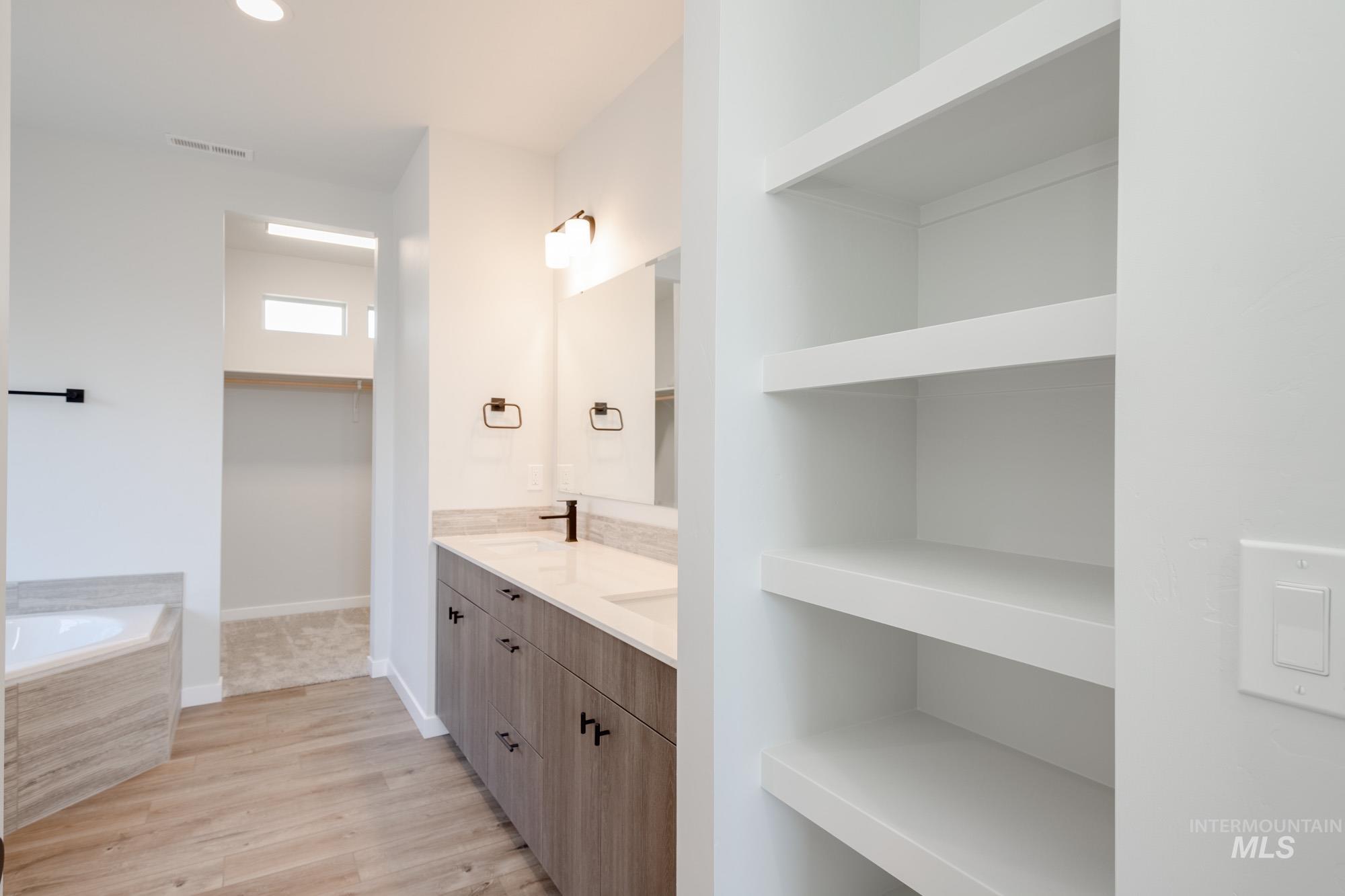 Bathroom featuring wood finished floors, double vanity, a bath, and recessed lighting