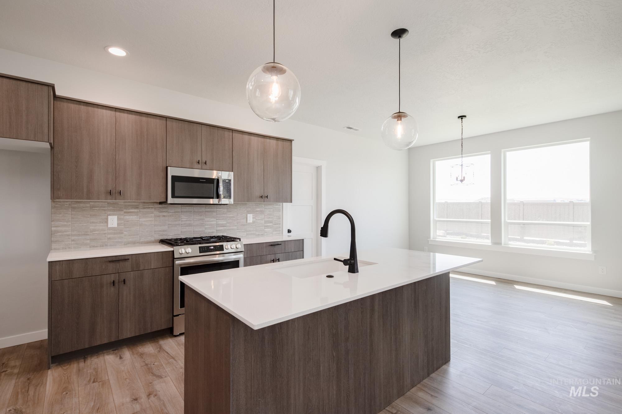 Kitchen with stainless steel appliances, backsplash, light countertops, and light wood finished floors