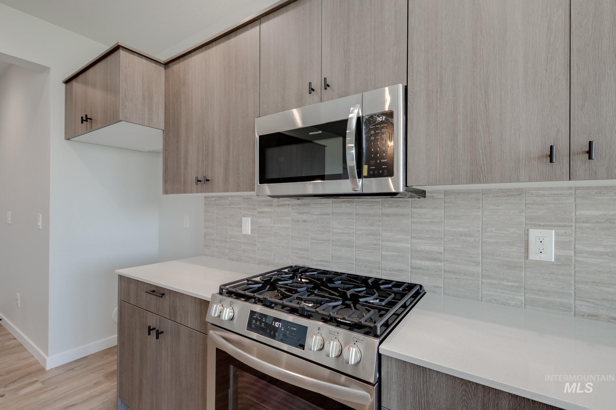 Kitchen featuring appliances with stainless steel finishes, light countertops, backsplash, light wood finished floors, and light brown cabinetry