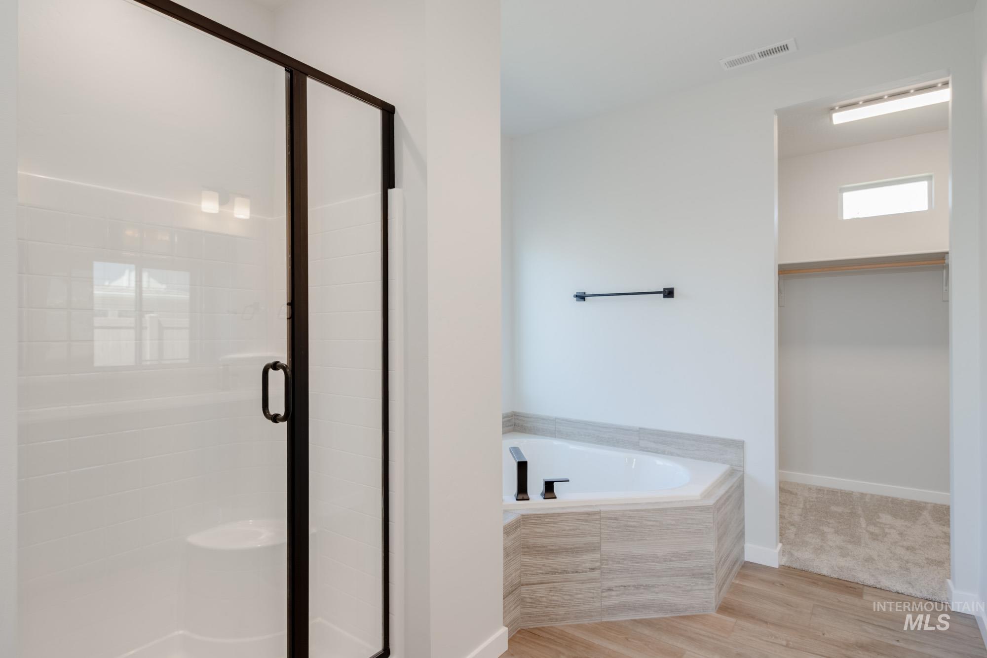 Full bathroom featuring wood finished floors, a stall shower, a garden tub, and a spacious closet