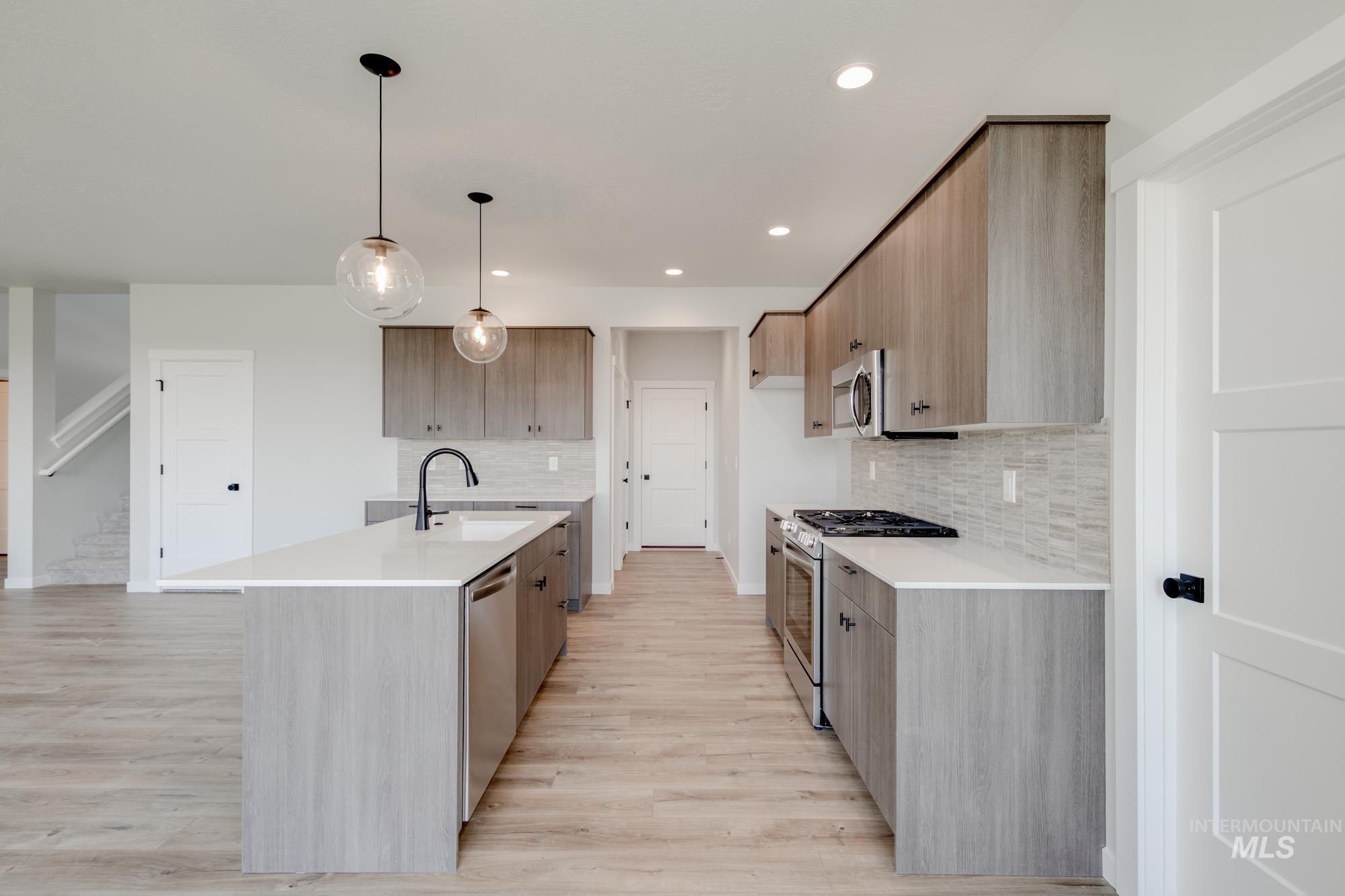 Kitchen with stainless steel appliances, light countertops, tasteful backsplash, recessed lighting, and light wood-style flooring