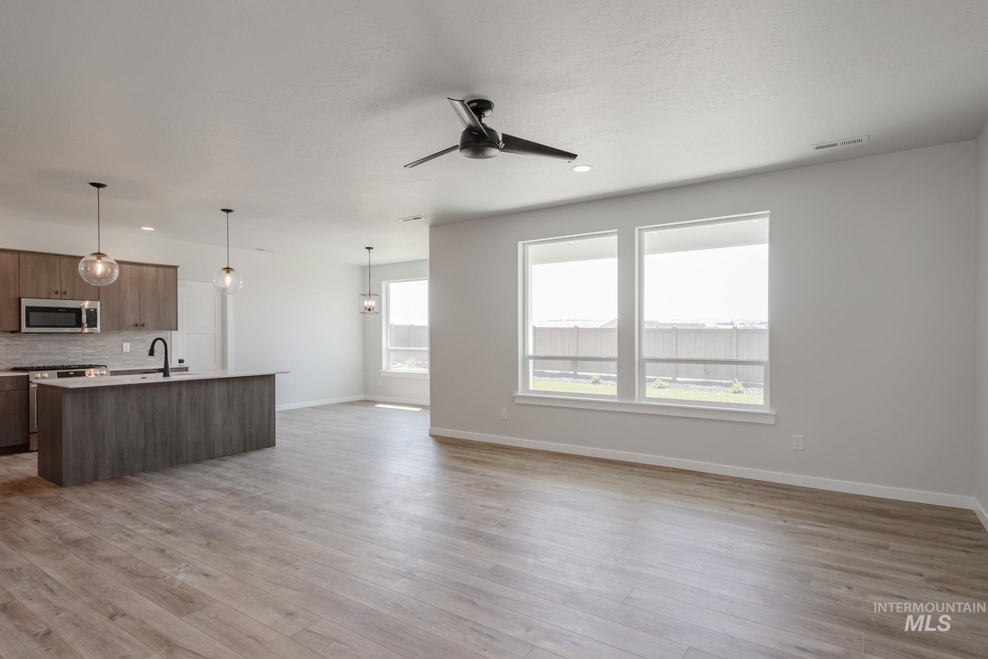 Kitchen with open floor plan, a ceiling fan, light wood-type flooring, an island with sink, and appliances with stainless steel finishes