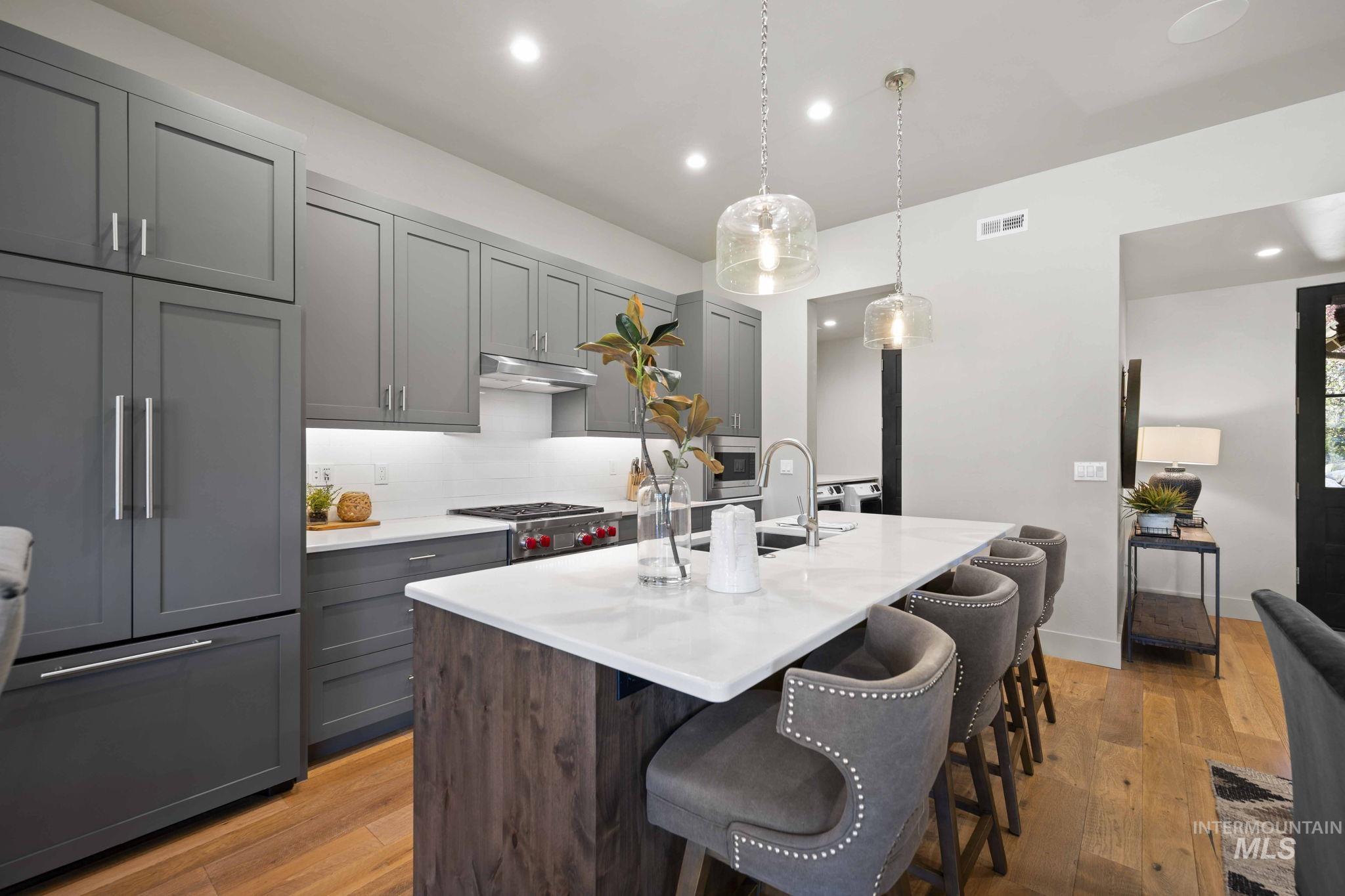 Kitchen with decorative light fixtures, light wood-type flooring, paneled built in fridge, a kitchen island with sink, and gray cabinetry