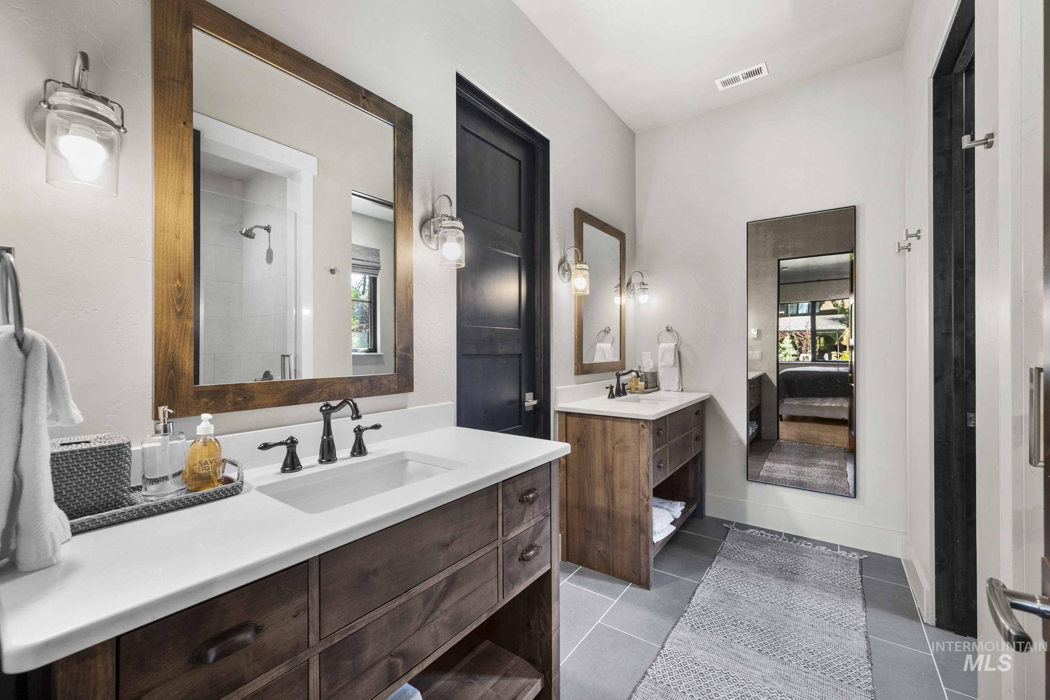 Full bath featuring dark tile patterned floors, two vanities, connected bathroom, and tiled shower