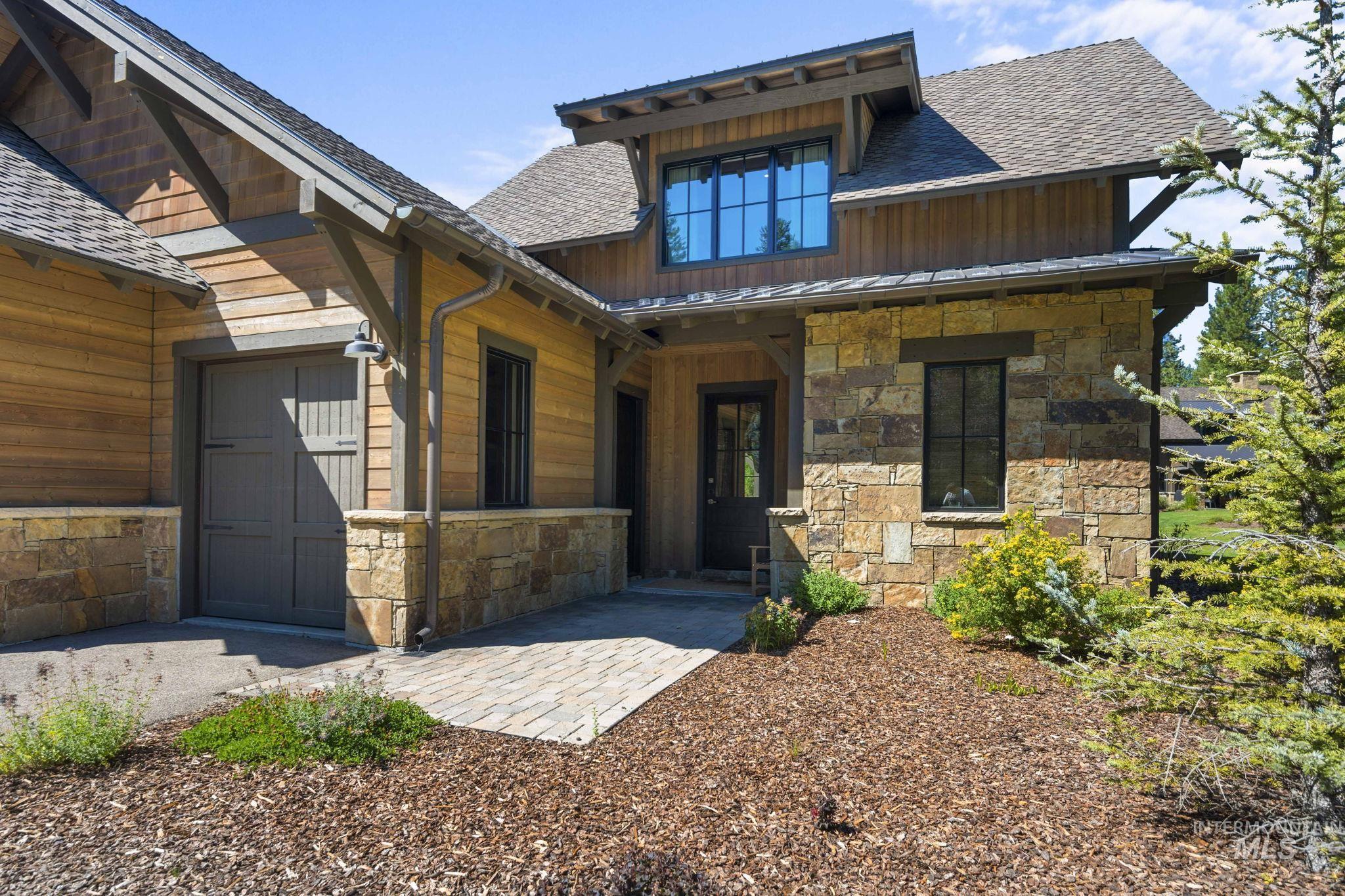 View of front of house with stone siding, roof with shingles, and a garage