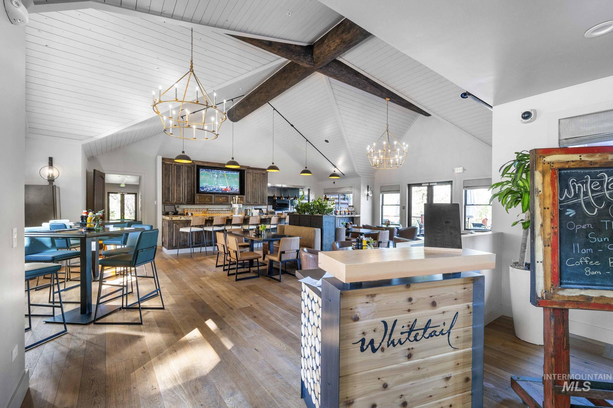 Dining room with a chandelier, hardwood / wood-style floors, high vaulted ceiling, beam ceiling, and healthy amount of natural light