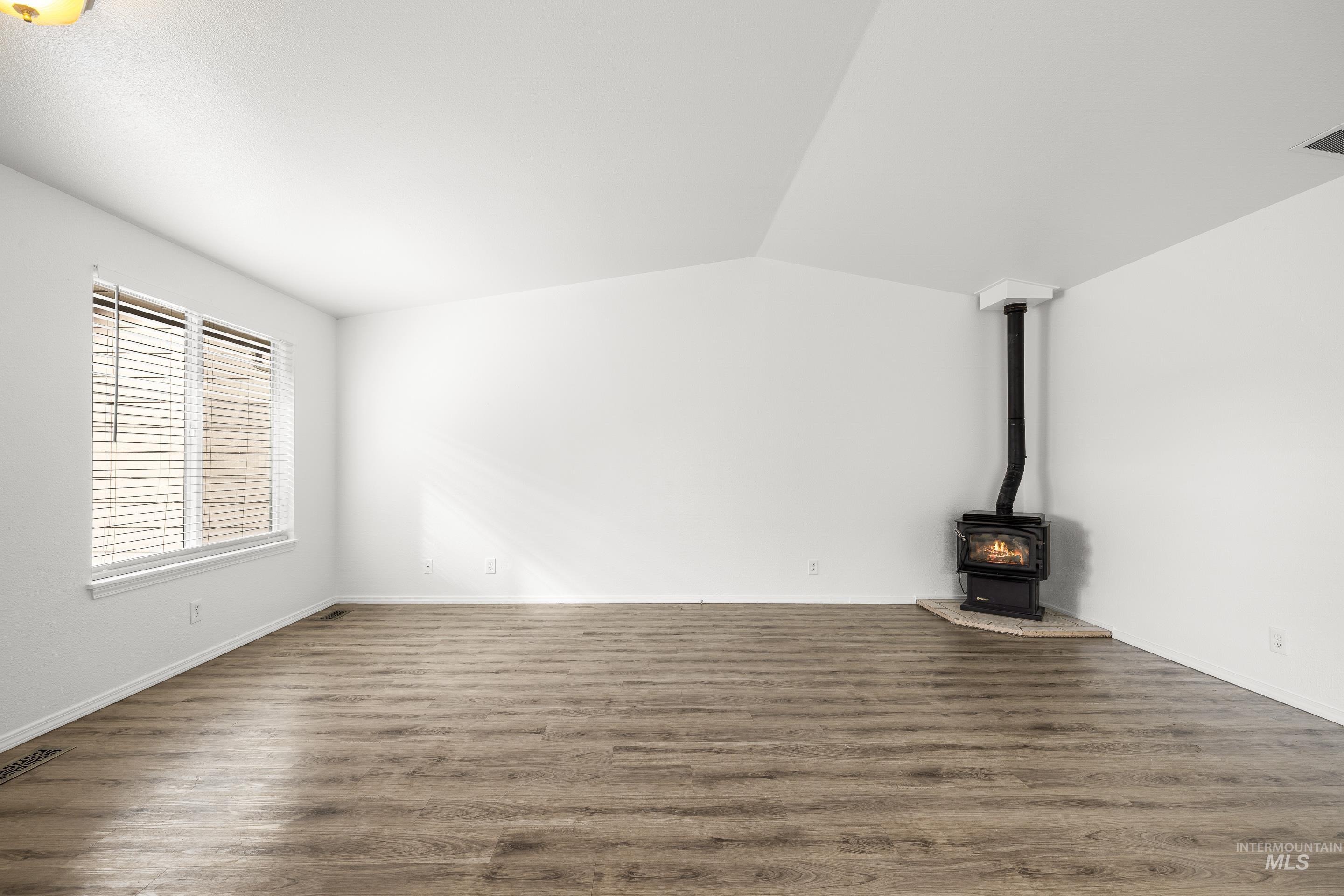 Unfurnished living room with a wood stove, dark wood-style flooring, and vaulted ceiling
