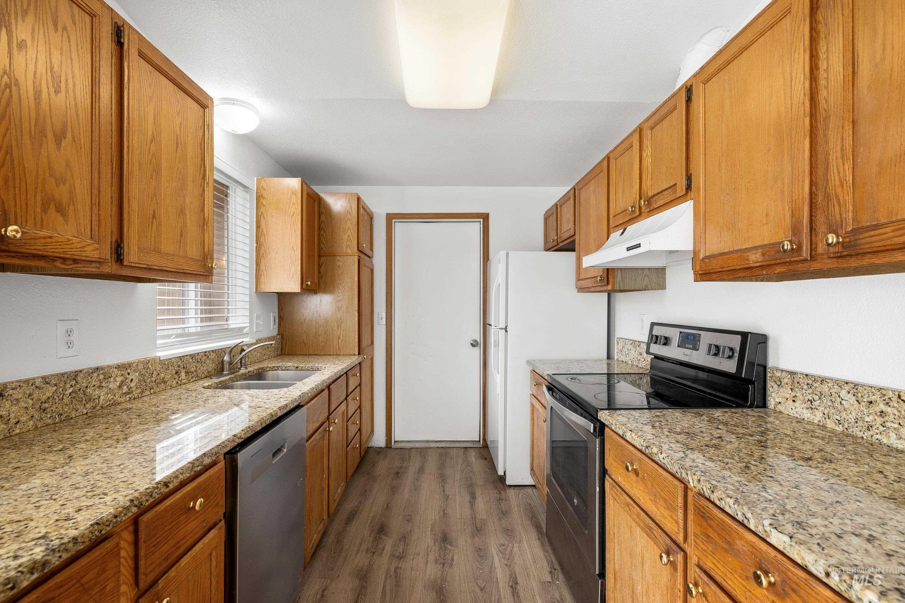 Kitchen with stainless steel appliances, dark wood-type flooring, wood finish cabinets, and light stone countertops