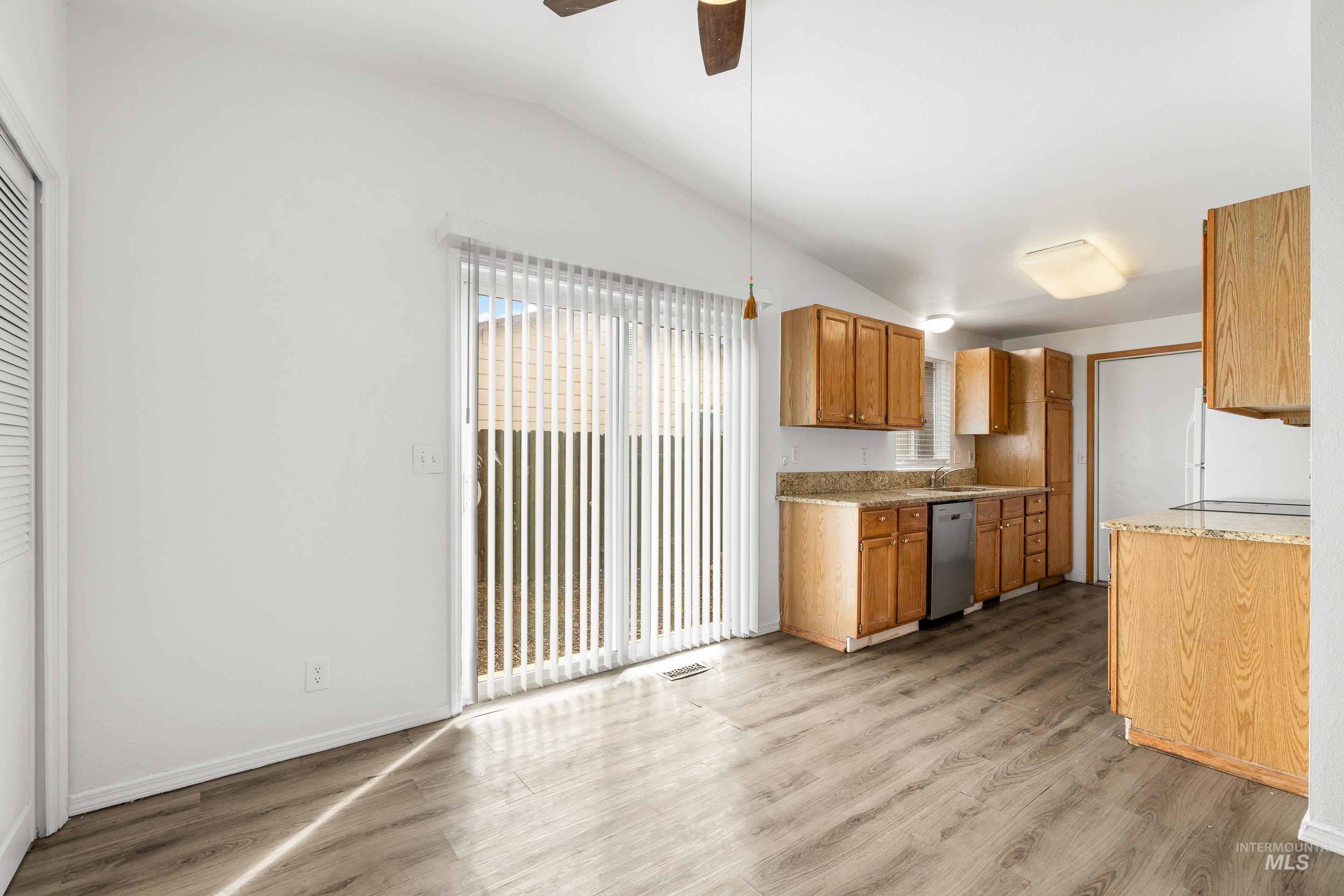 Kitchen with vaulted ceiling, light wood-type flooring, ceiling fan, freestanding refrigerator, and stainless steel dishwasher
