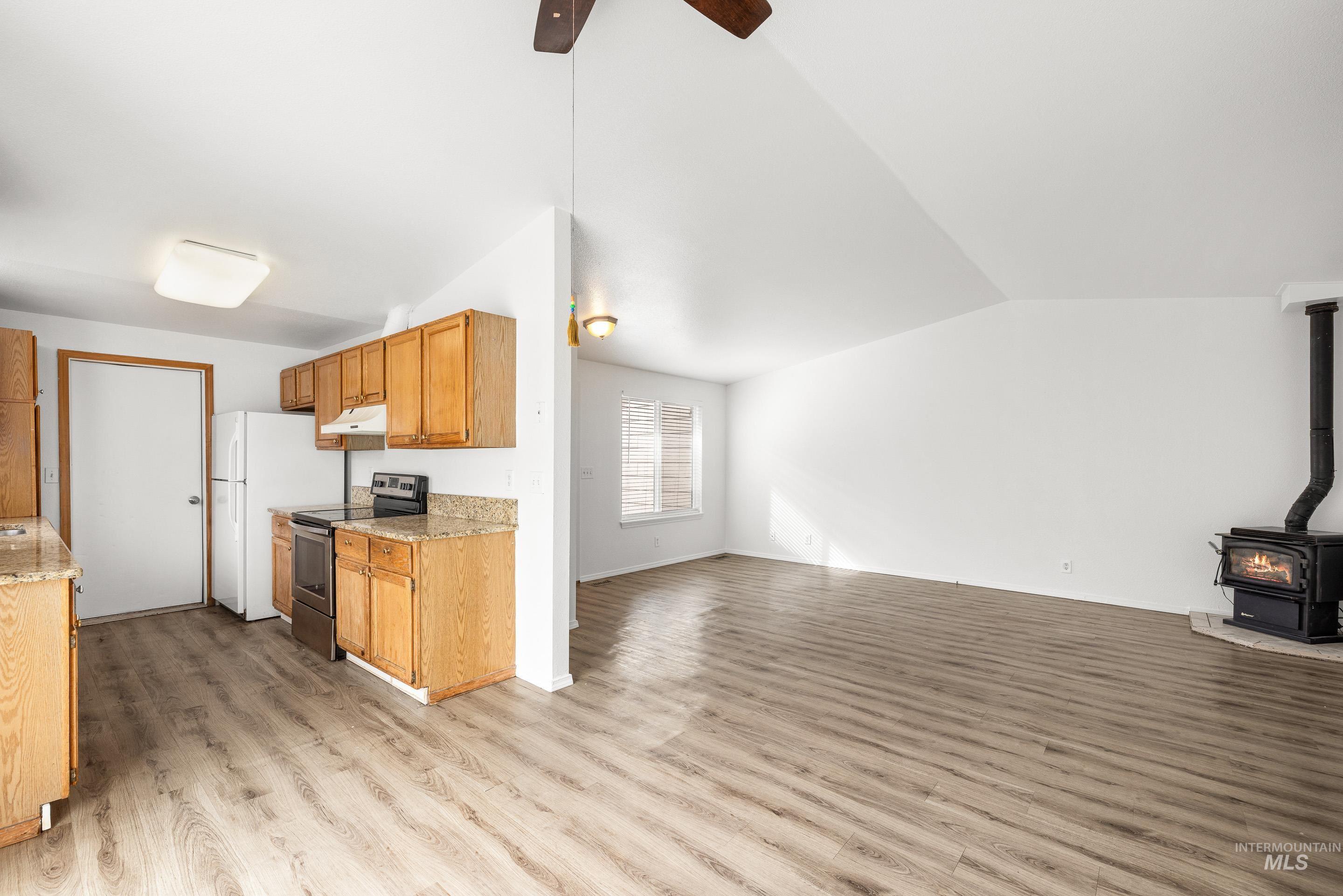 Kitchen featuring stainless steel range with electric stovetop, a wood stove, open floor plan, light wood-style floors, and a ceiling fan