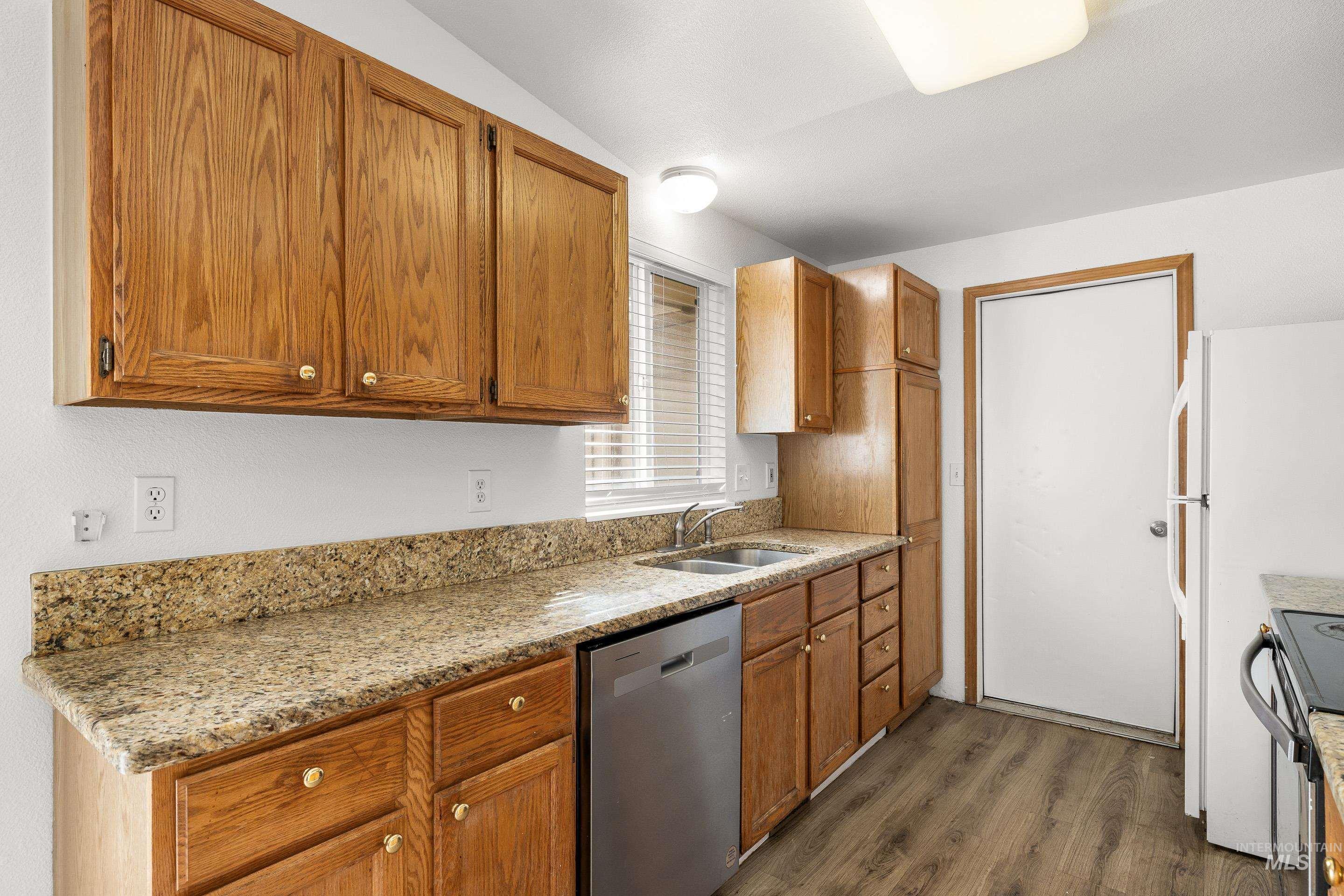 Kitchen featuring stainless steel dishwasher, wood finish cabinetry, light stone counters, dark wood finished floors, and lofted ceiling