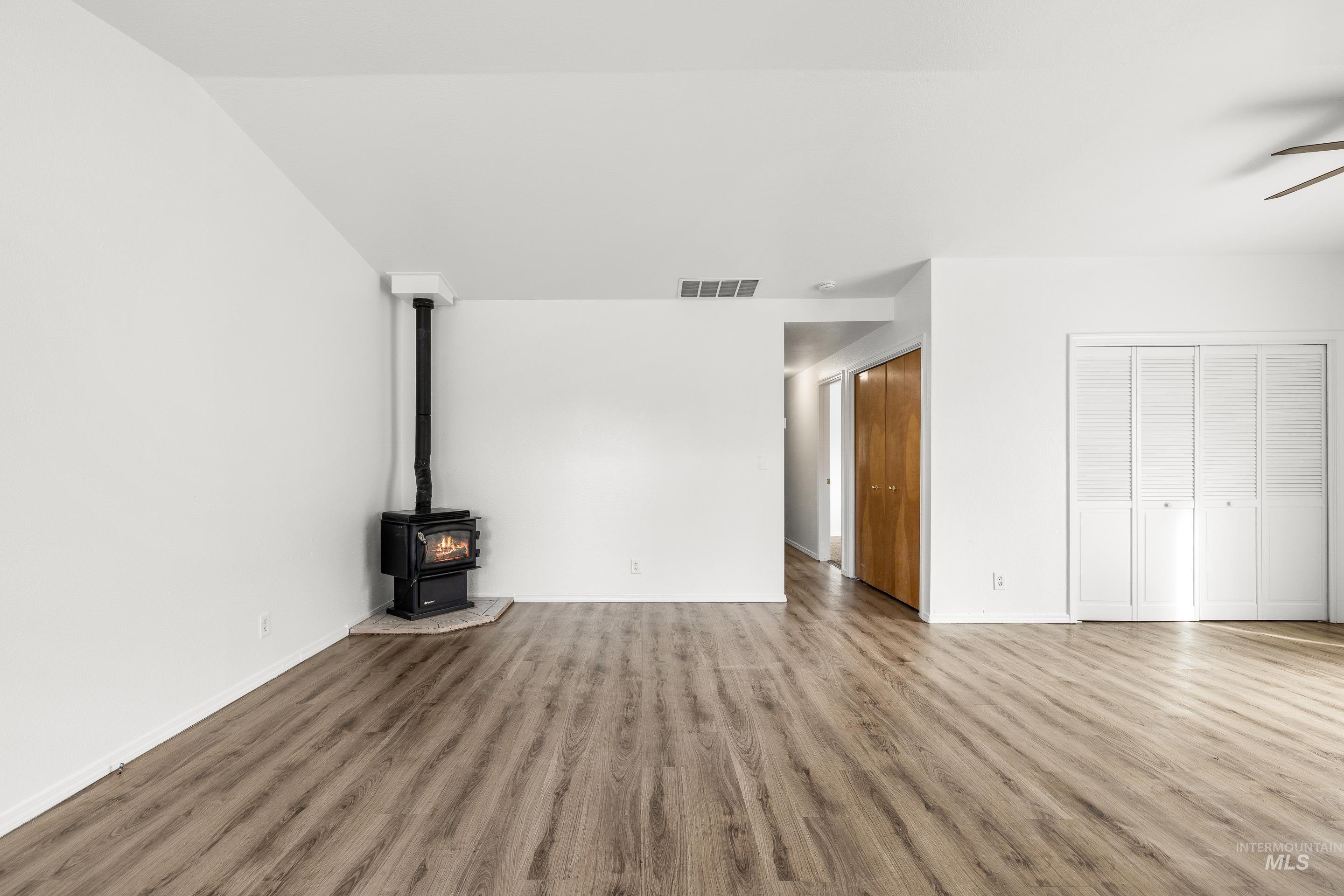 Unfurnished living room with a wood stove, wood finished floors, and ceiling fan