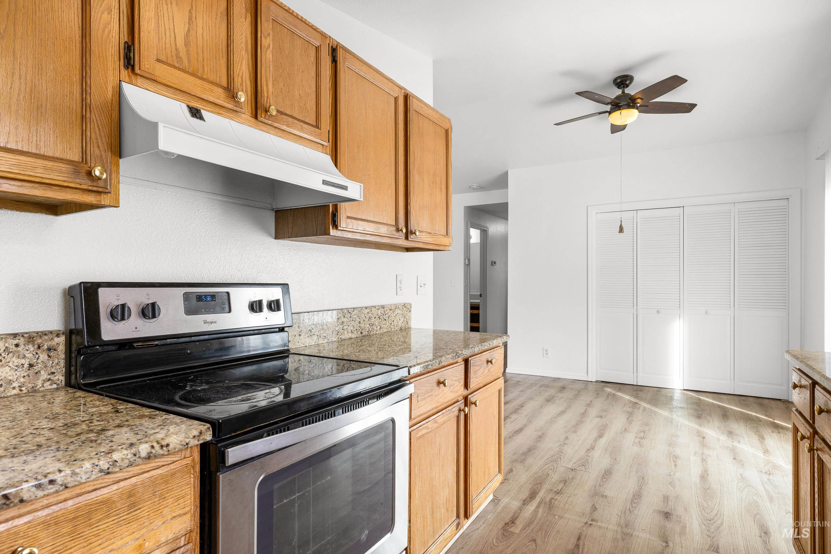 Kitchen with stainless steel range with electric stovetop, ceiling fan, light stone counters, light wood-type flooring, and wood finish cabinetry