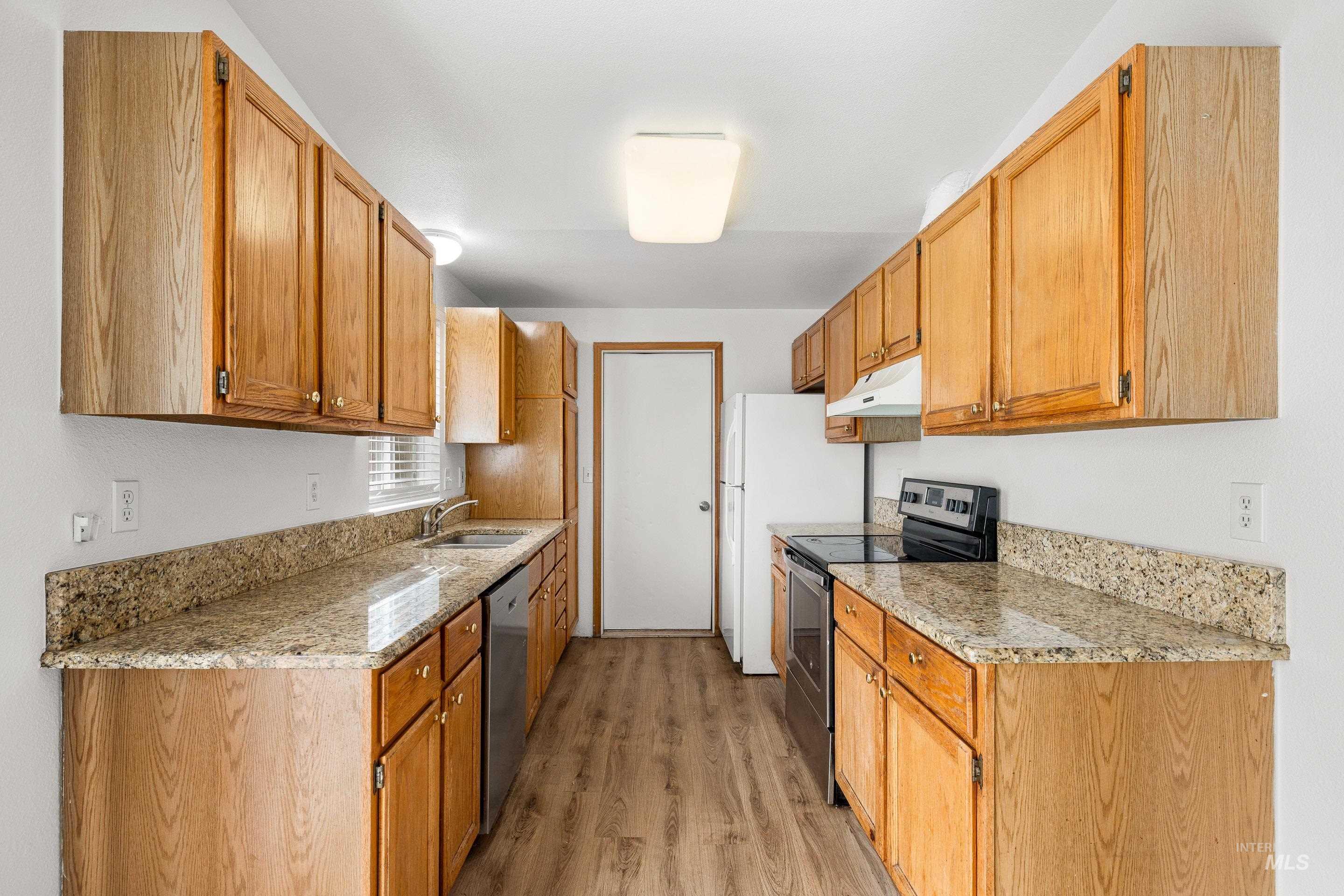 Kitchen with stainless steel appliances, light stone countertops, light wood-style floors, and wood finish cabinetry