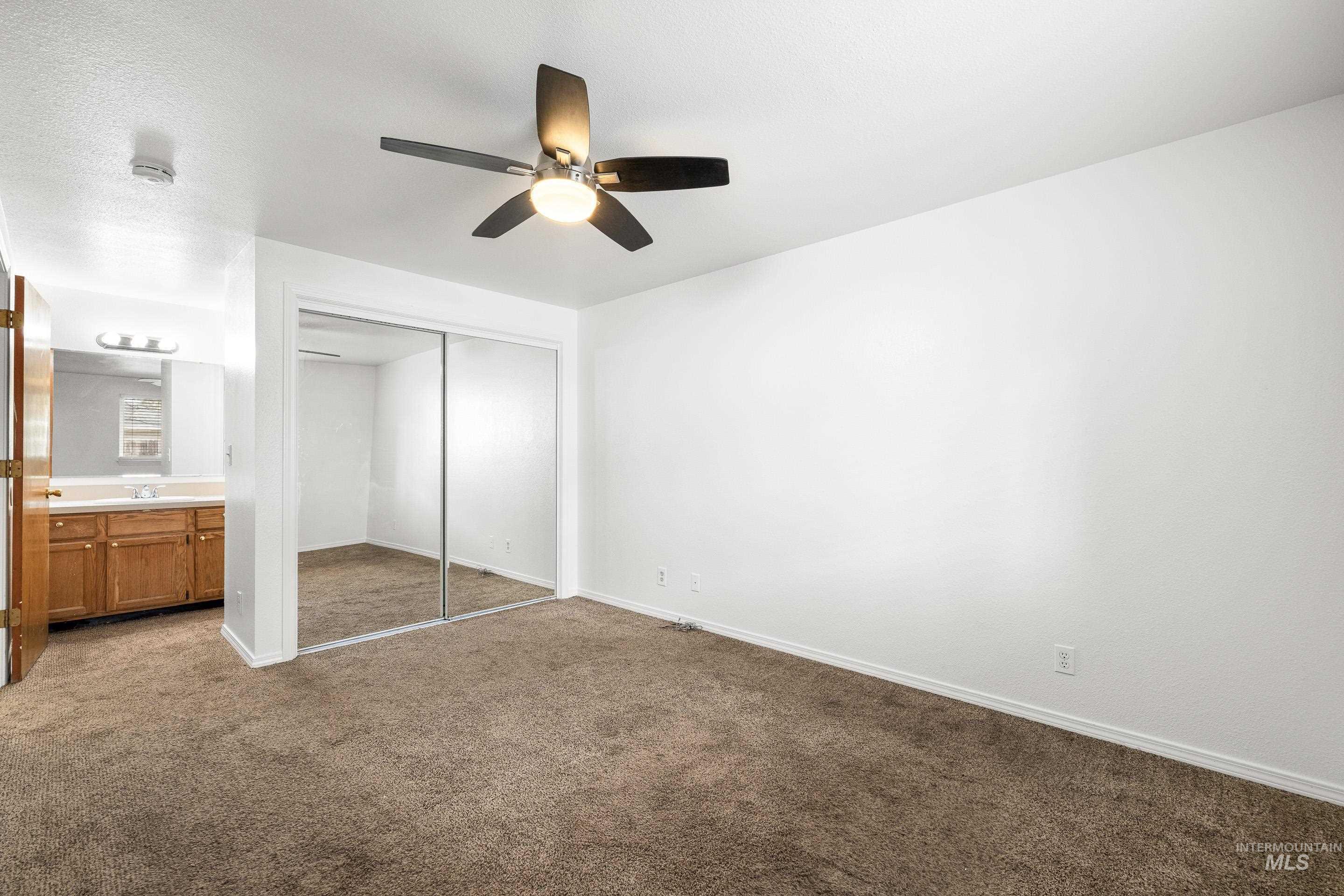 Unfurnished bedroom with dark carpet, ensuite bath, a closet, and ceiling fan