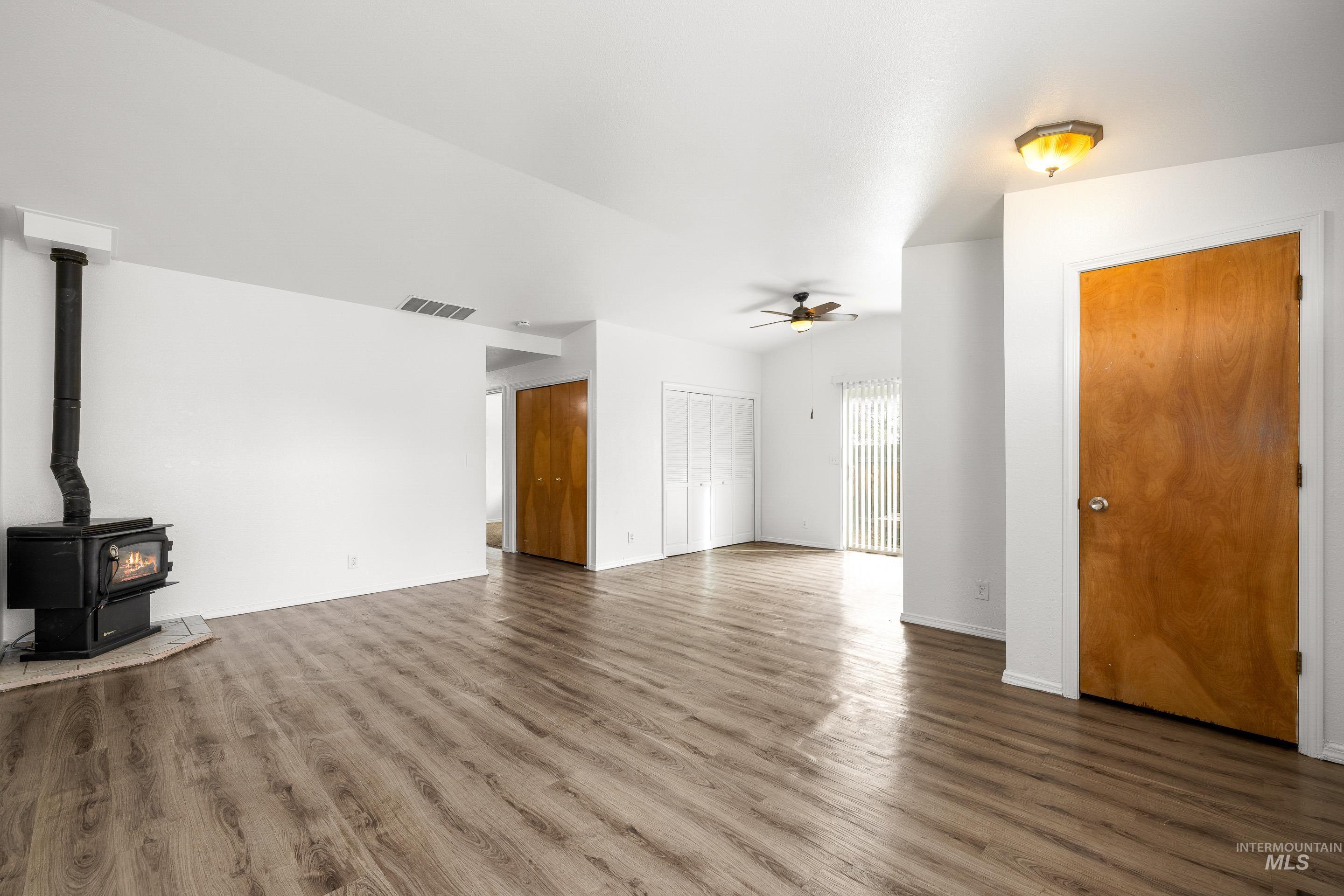Unfurnished living room featuring dark wood-type flooring, ceiling fan, and a wood stove