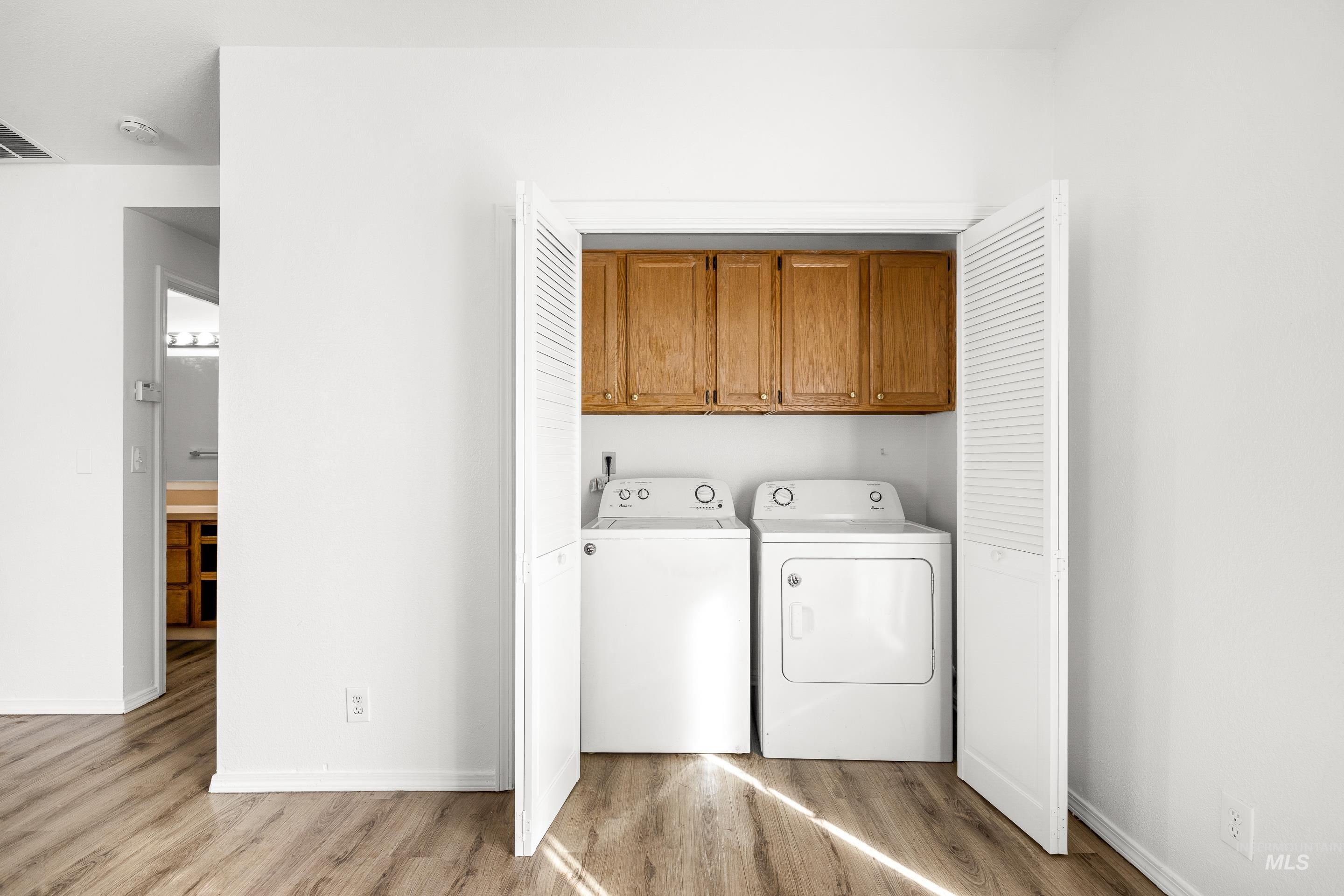 Laundry area featuring washing machine and dryer, light wood-style floors, and cabinet space