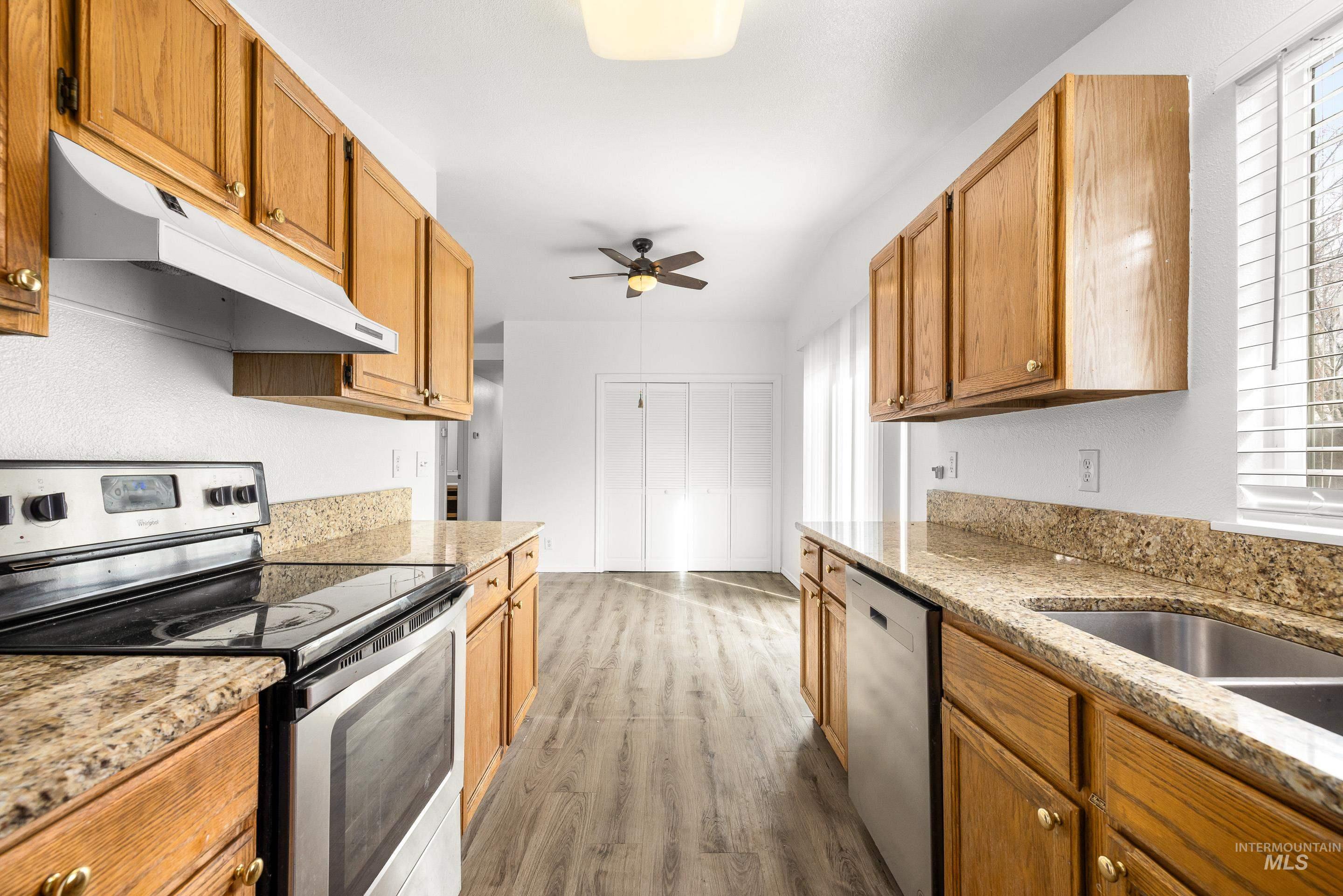 Kitchen featuring stainless steel appliances, light stone countertops, dark wood-style flooring, and ceiling fan