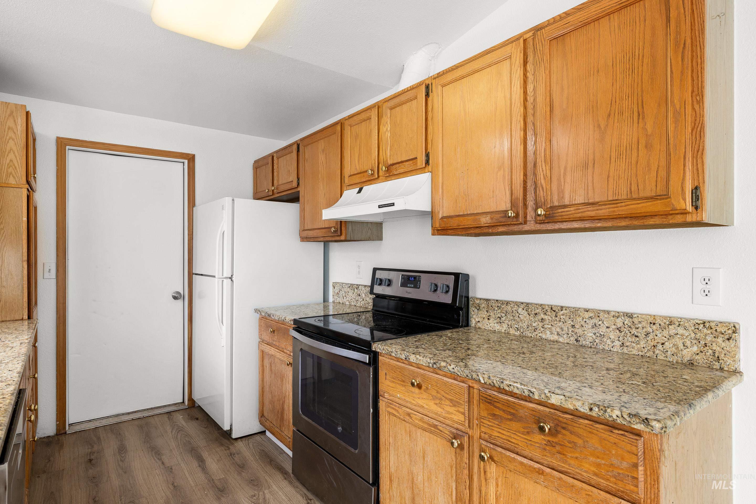 Kitchen with electric range, dark wood-type flooring, light stone counters, freestanding refrigerator, and wood finish cabinetry