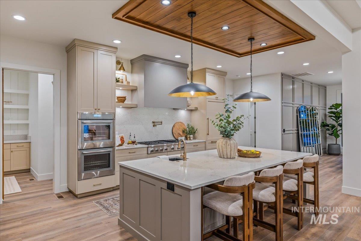 Kitchen featuring gray cabinetry, light stone countertops, decorative light fixtures, open shelves, and a kitchen bar