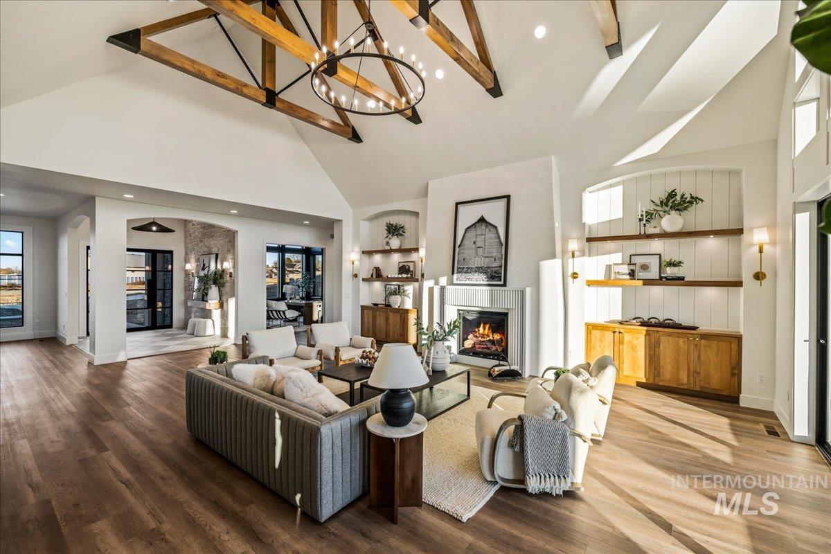Living room featuring a glass covered fireplace, high vaulted ceiling, wood finished floors, recessed lighting, and a chandelier