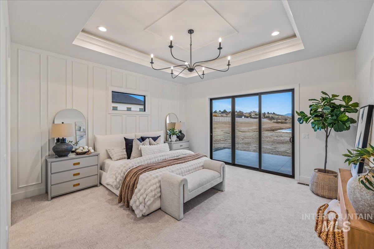Bedroom featuring light carpet, a tray ceiling, access to outside, a decorative wall, and a chandelier