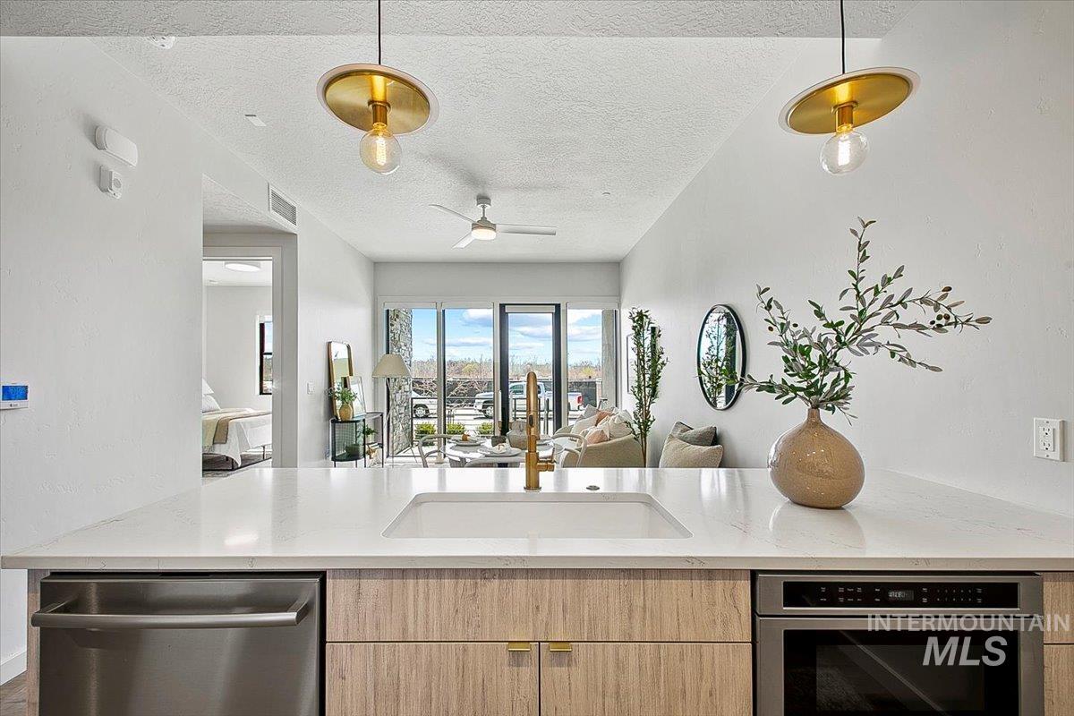 Kitchen featuring light brown cabinets, open floor plan, light stone countertops, stainless steel appliances, and a textured ceiling