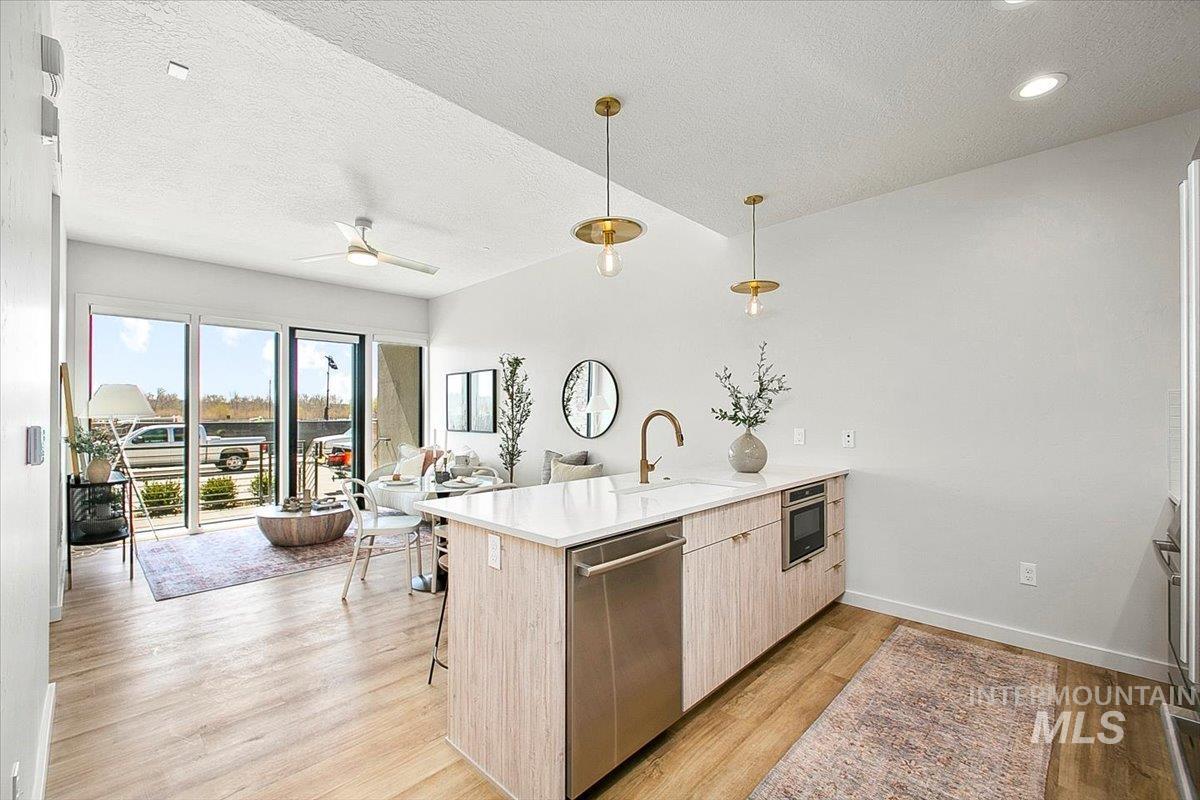 Kitchen featuring a peninsula, modern cabinets, pendant lighting, stainless steel dishwasher, and light wood finished floors