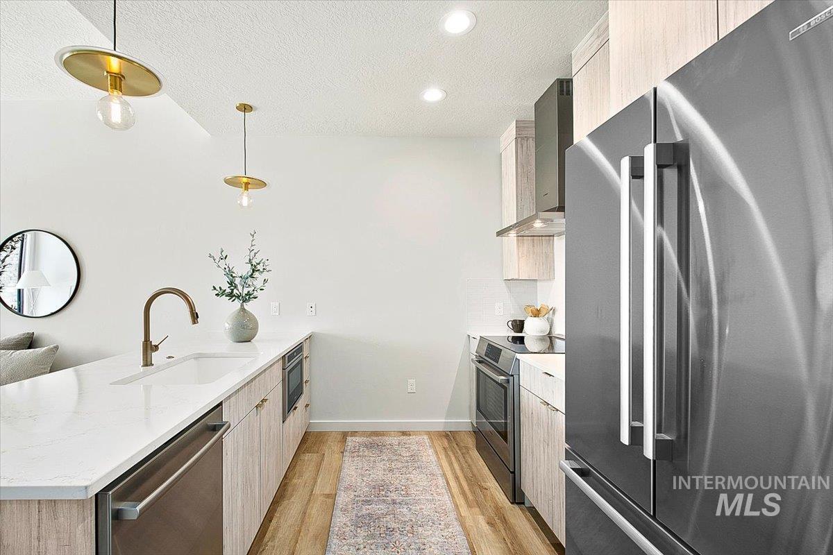 Kitchen with stainless steel appliances, a peninsula, light wood-type flooring, modern cabinets, and wall chimney exhaust hood