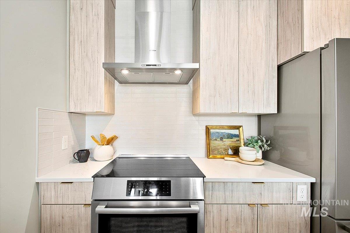 Kitchen featuring wall chimney exhaust hood, light brown cabinets, stainless steel appliances, and modern cabinets