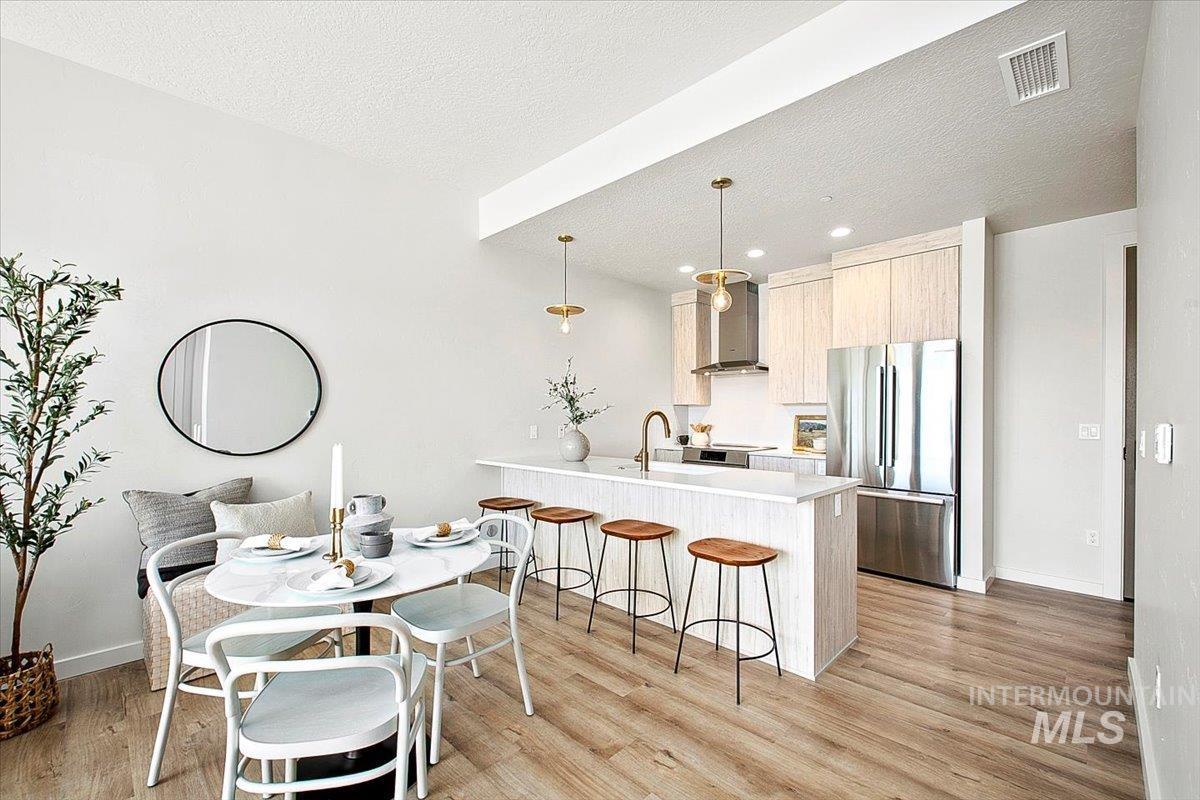 Kitchen featuring freestanding refrigerator, a peninsula, light brown cabinets, pendant lighting, and light wood finished floors