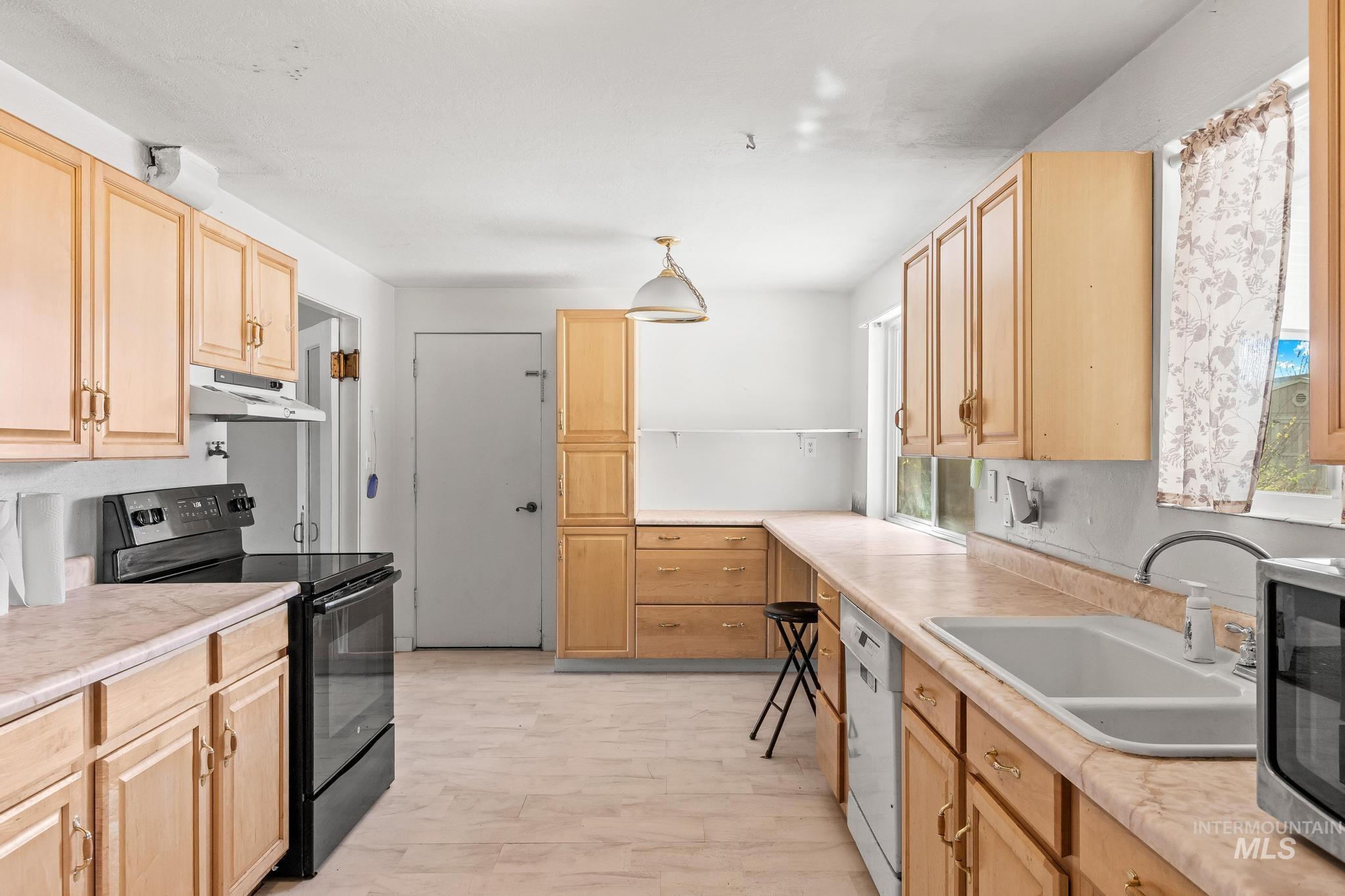 Kitchen featuring black electric range oven, light brown cabinetry, and light countertops