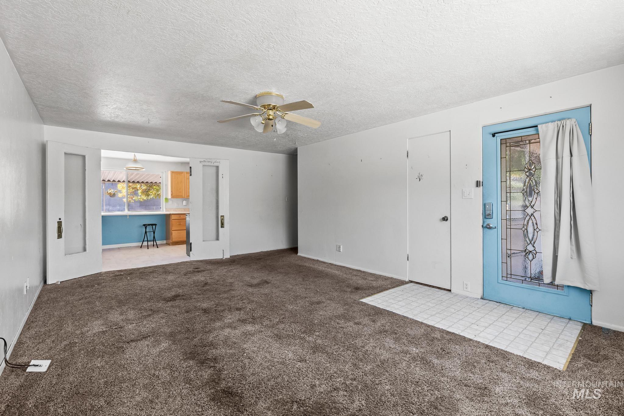 Unfurnished living room featuring a textured ceiling, carpet, and ceiling fan