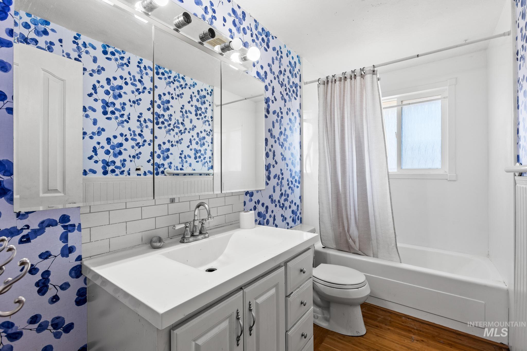 Full bath featuring shower / bath combo with shower curtain, dark wood-style floors, vanity, and decorative backsplash