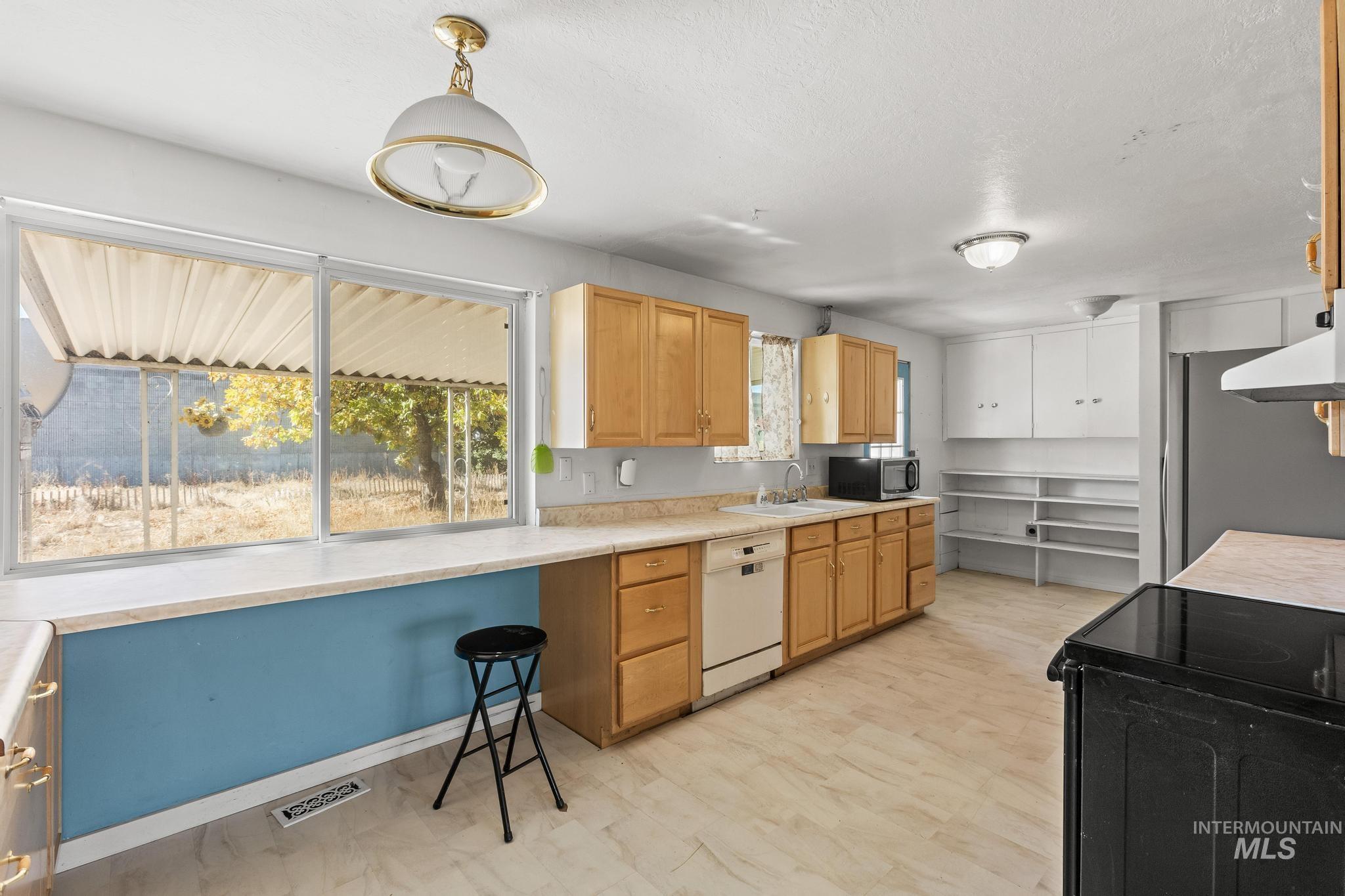 Kitchen with black appliances, light countertops, decorative light fixtures, light brown cabinetry, and extractor fan