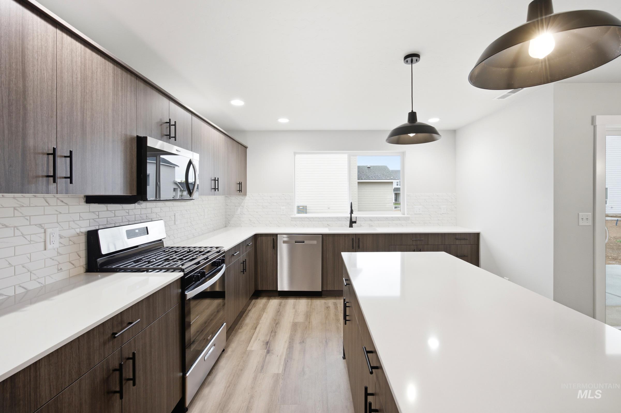 Modern kitchen featuring a spacious island, white countertops, wood-finish cabinetry with matte black hardware, stainless steel appliances, and a tiled backsplash