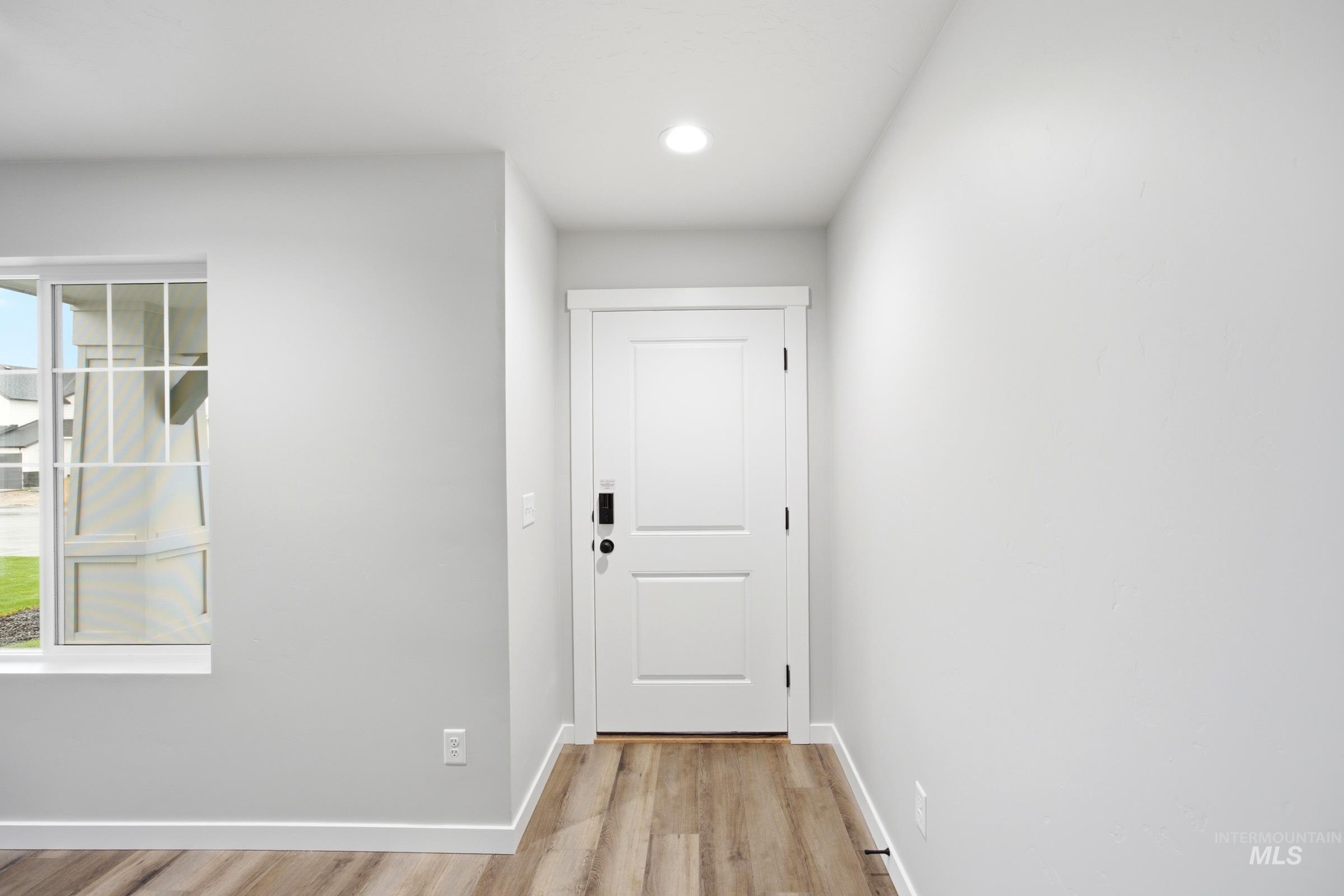 Entryway featuring wood-finish flooring, white paneled door, and recessed lighting
