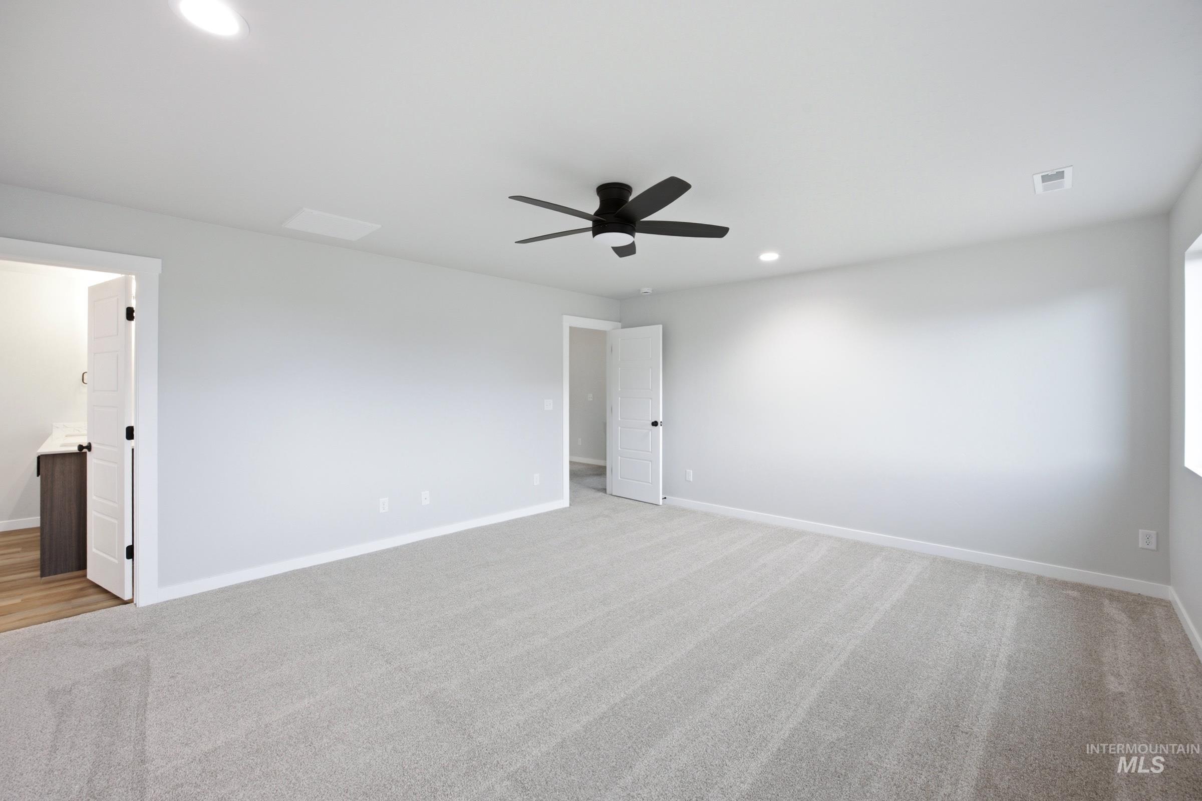 Spacious room featuring light gray carpeting, neutral wall finishes, and a contemporary black ceiling fan