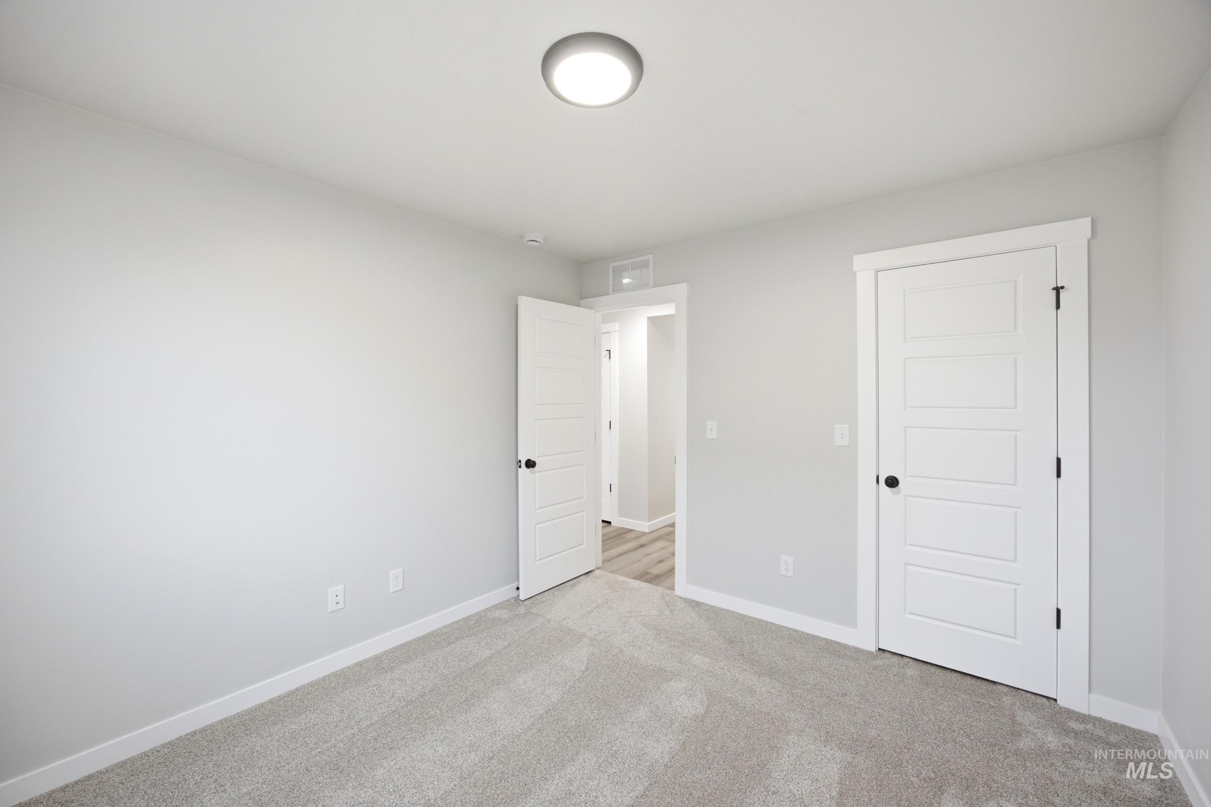 Spacious room featuring light gray walls, plush gray carpeting, and white trim