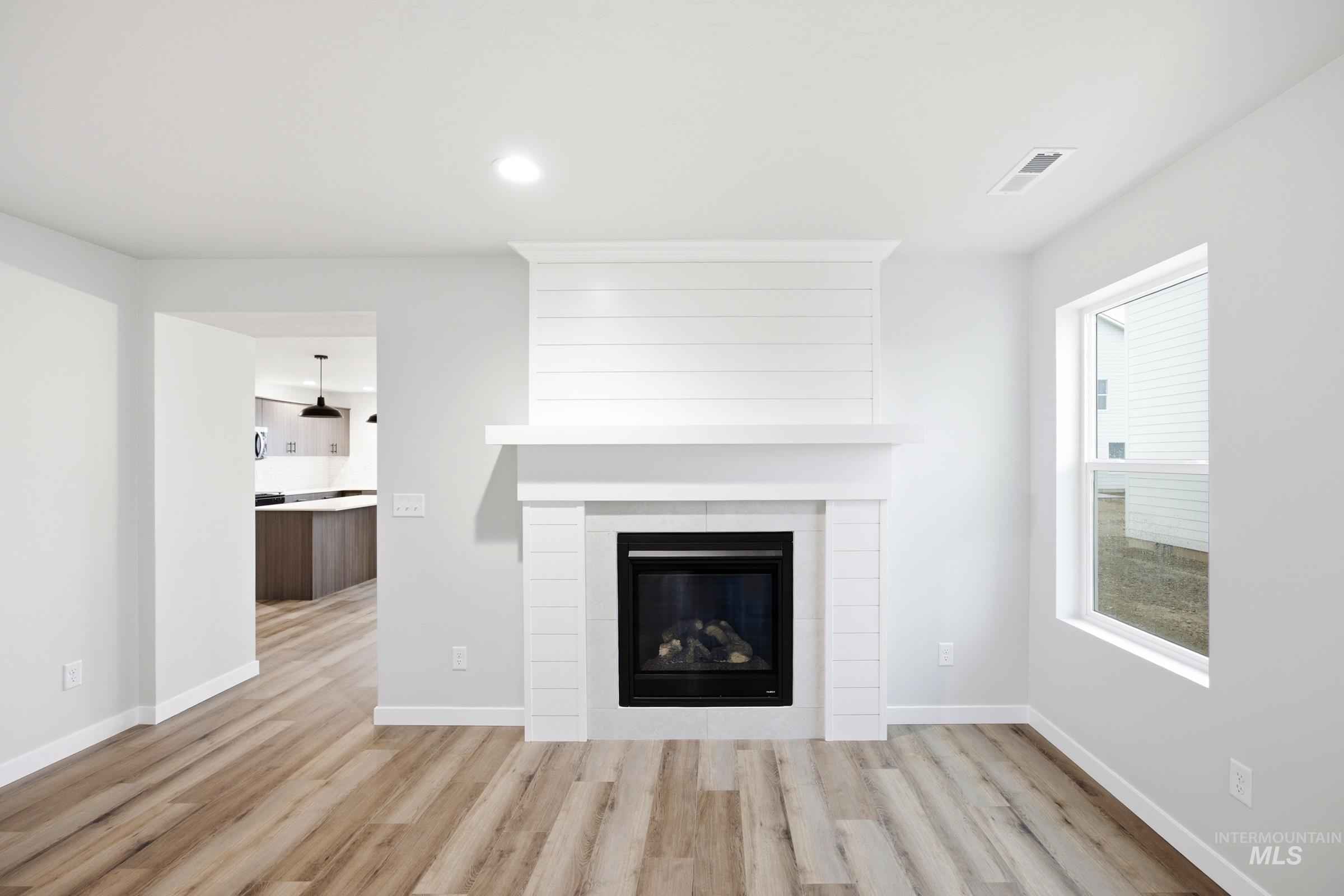White shiplap fireplace with a black insert, wood-finish flooring, a bright window, and recessed lighting