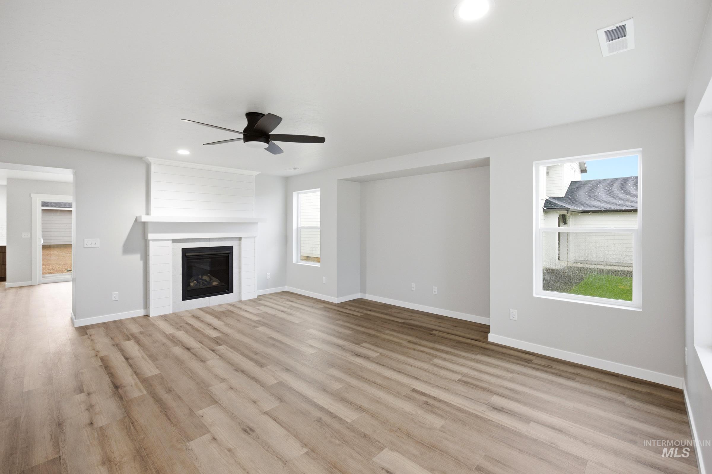 Spacious living area featuring wood-finish flooring, a shiplap-accented fireplace, a ceiling fan, recessed lighting, and multiple windows
