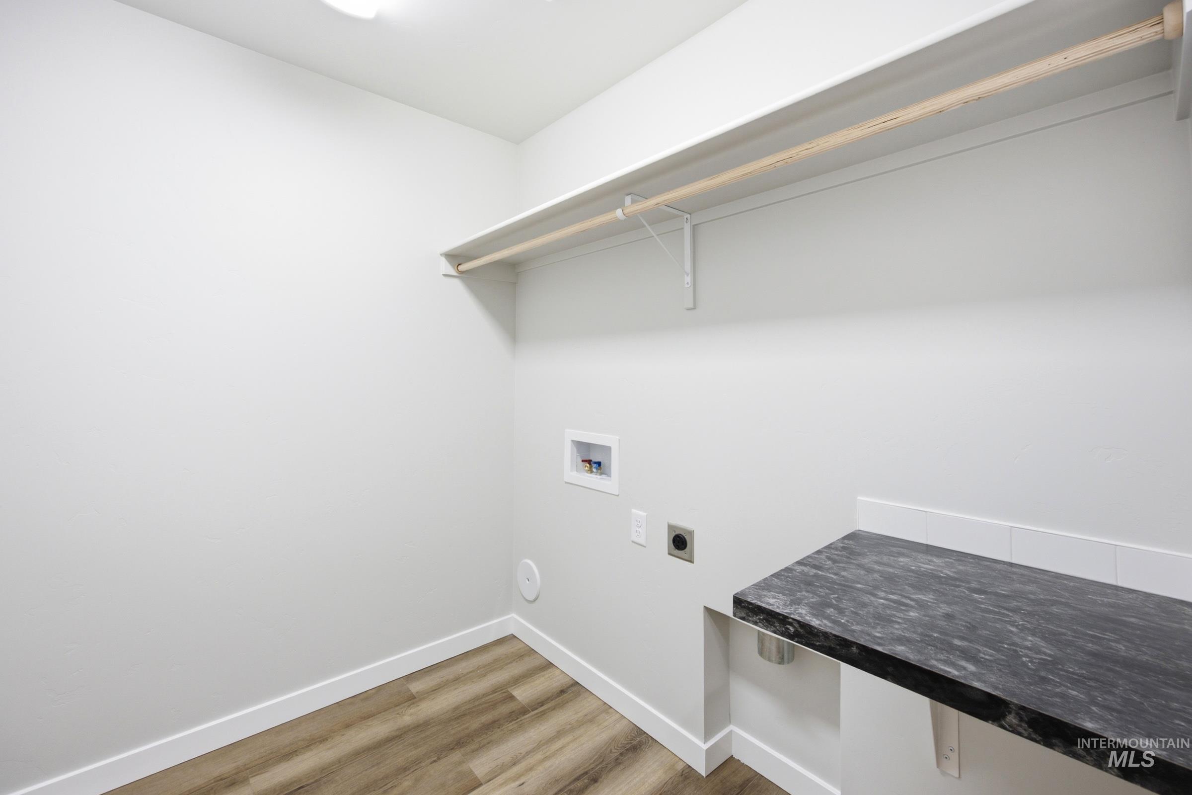 Dedicated laundry area featuring wood-finish flooring, a dark stone-look countertop, white subway tile backsplash, and an overhead clothes rod