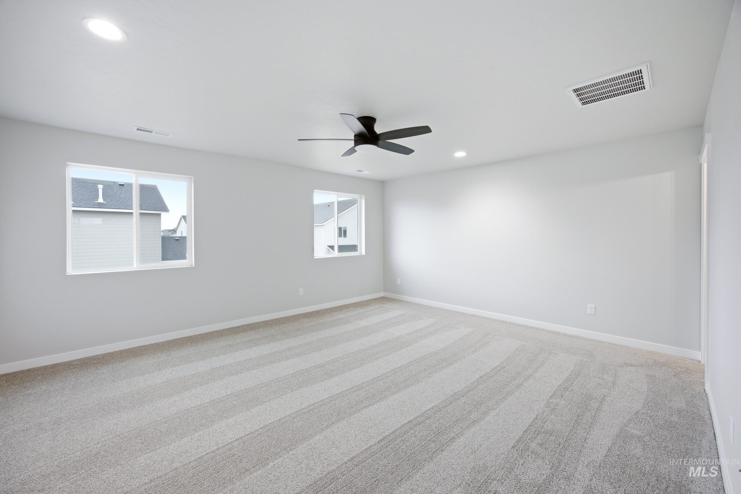 Spacious room featuring light-toned walls, patterned carpeting, two windows, recessed lighting, and a ceiling fan