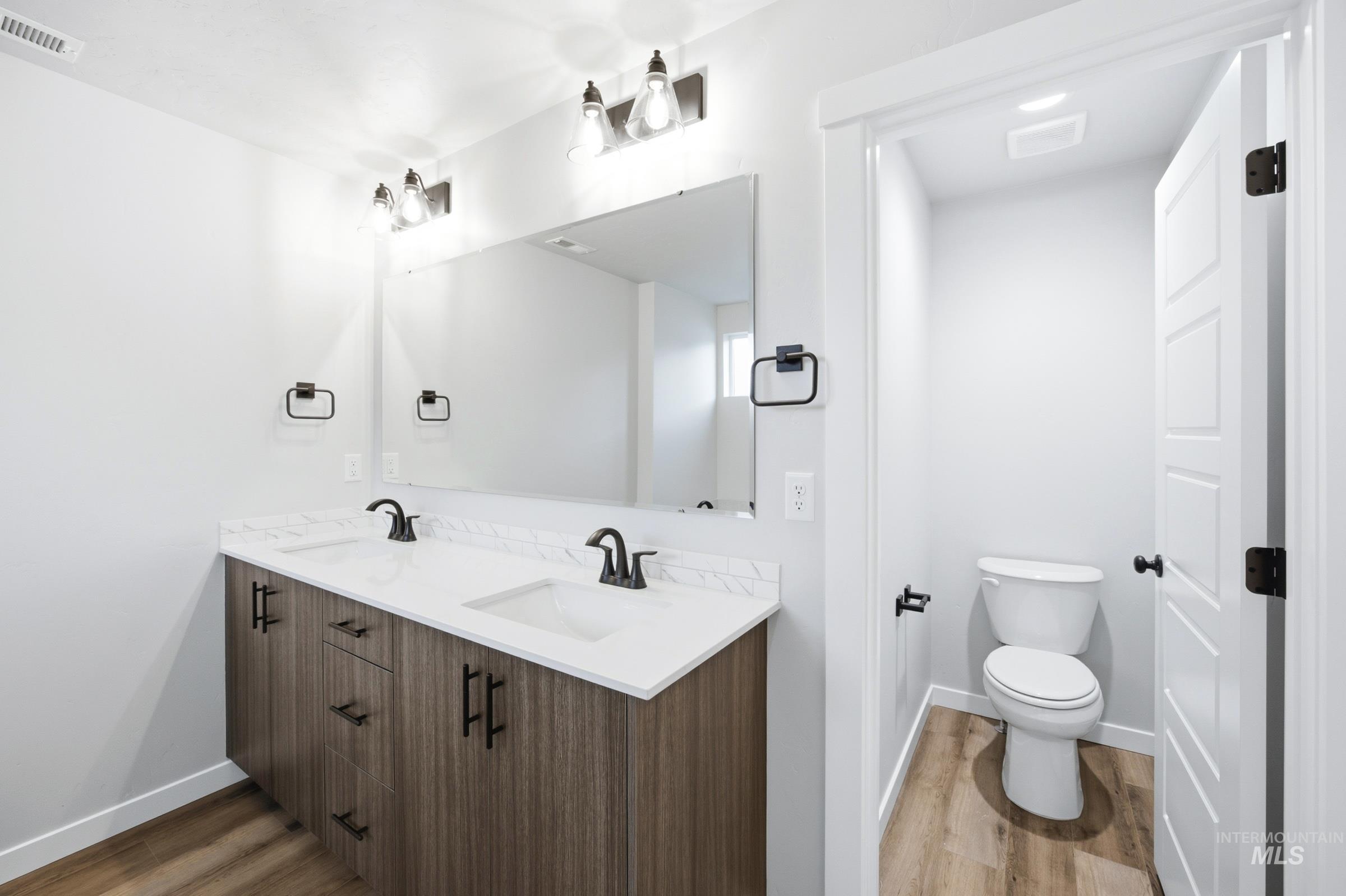 Dual vanity with wood-finish cabinetry, white countertops, and matte black fixtures