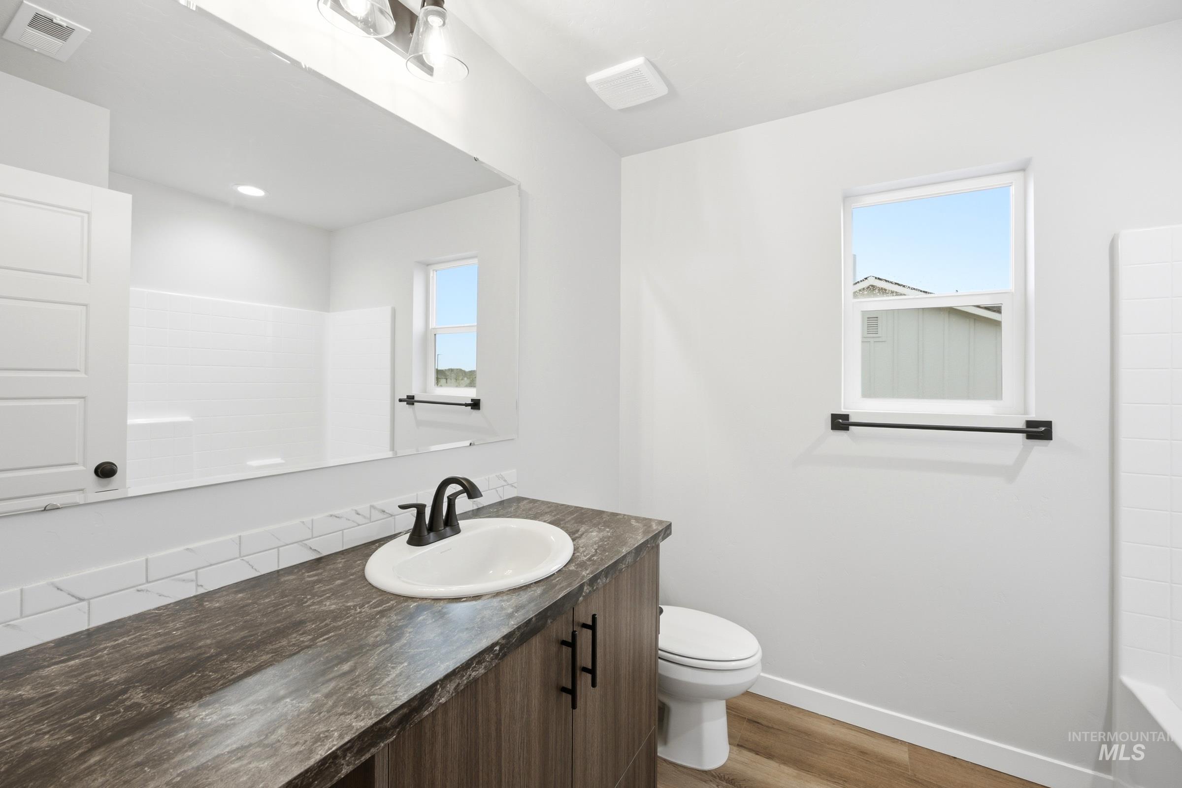 Bathroom featuring a wood-finish vanity with a white oval sink, matte black faucet, and a large mirror