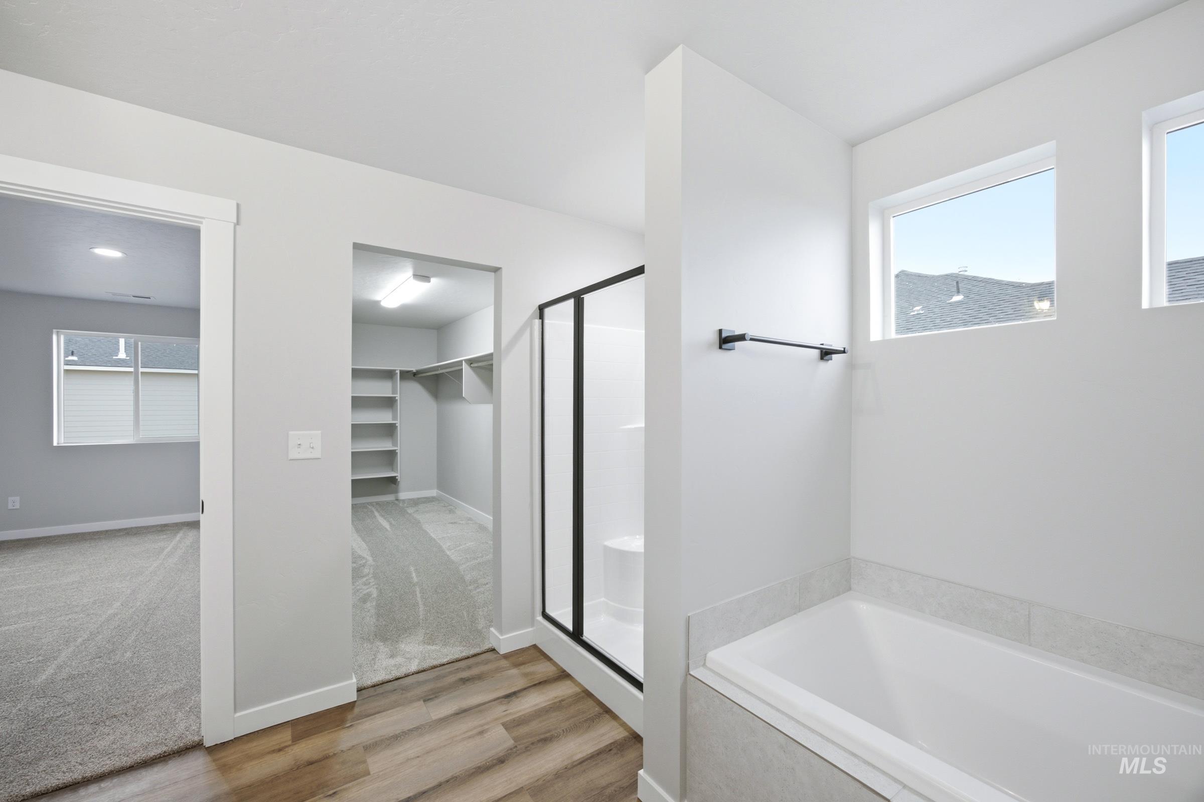 Bathroom featuring a walk-in shower with black-framed glass enclosure, a white soaking tub, and wood-finish flooring