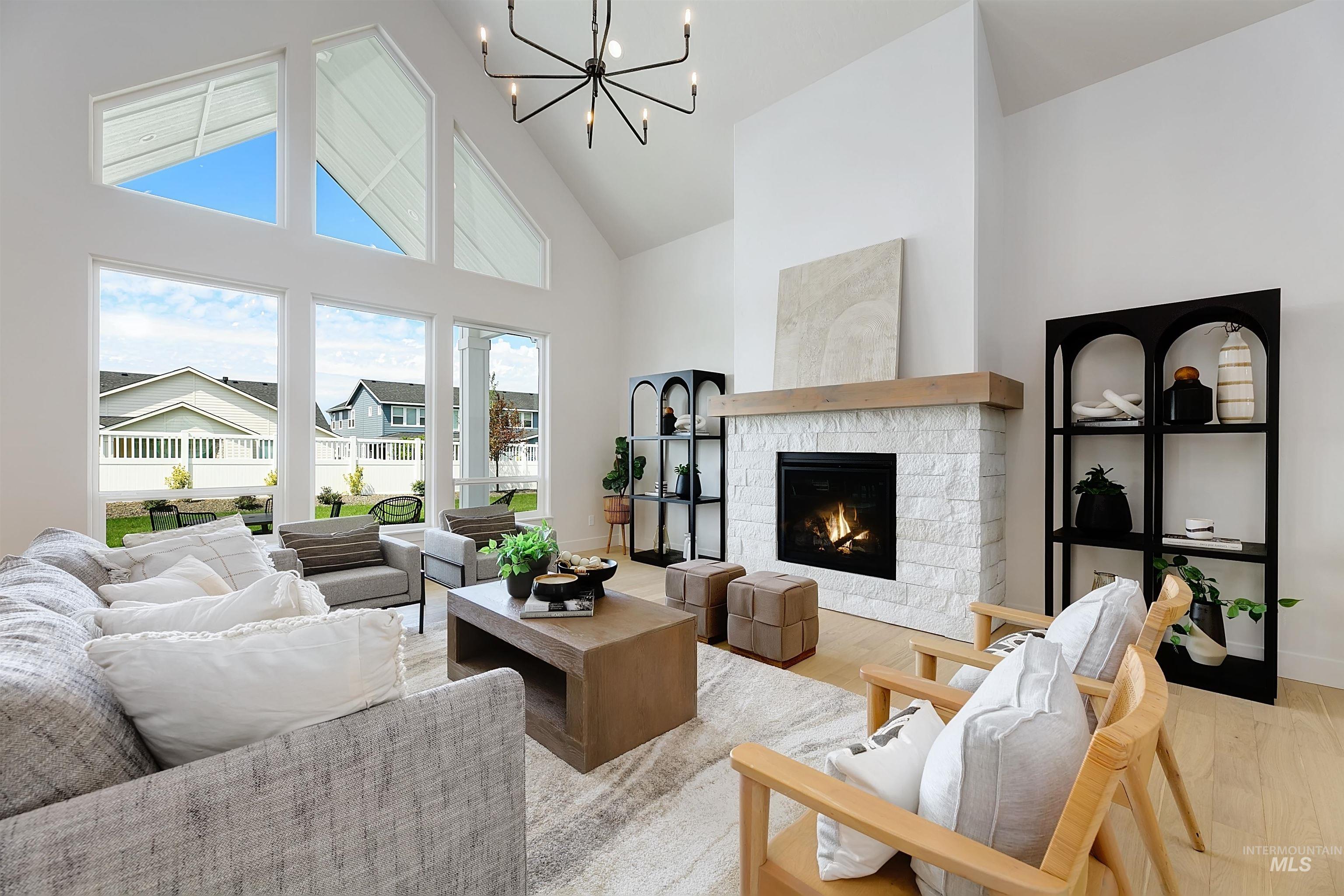 Living area featuring high vaulted ceiling, wood finished floors, a warm lit fireplace, and a chandelier