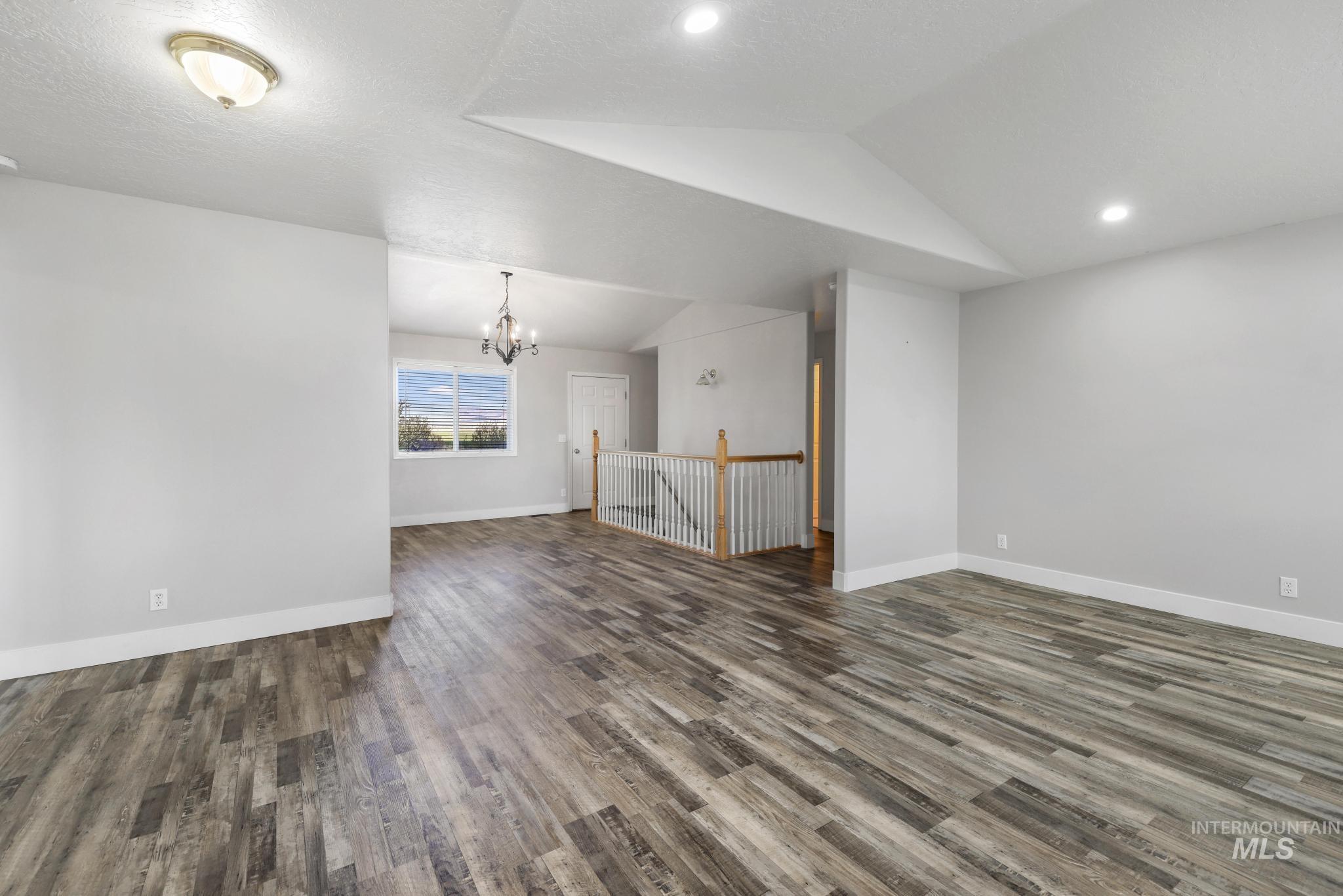 Spare room featuring vaulted ceiling, dark wood-type flooring, and a chandelier