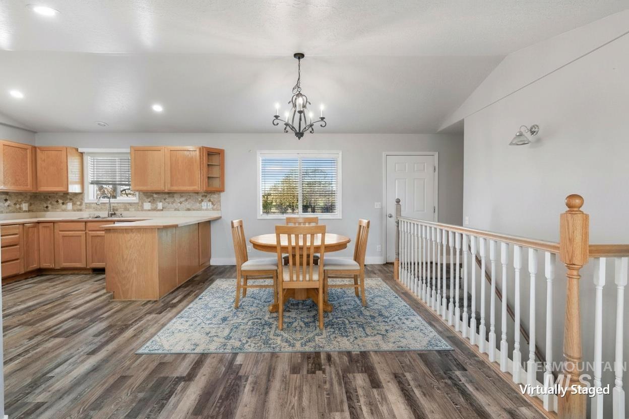 Open-concept living space with wood-finish flooring, a kitchen featuring wood cabinetry and a tile backsplash, and a dining area illuminated by a chandelier