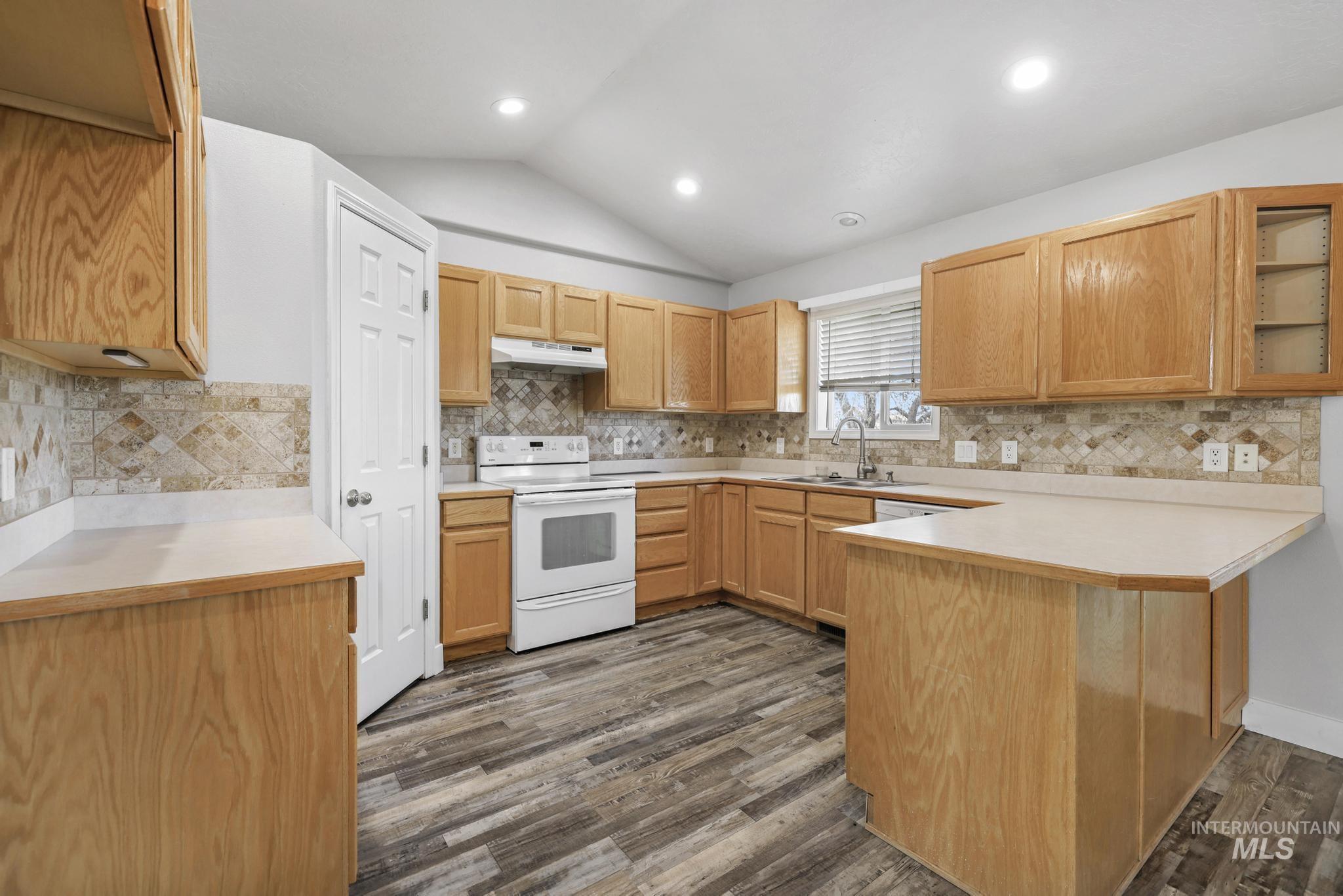 Kitchen featuring a peninsula, light countertops, white electric stove, vaulted ceiling, and dark wood finished floors